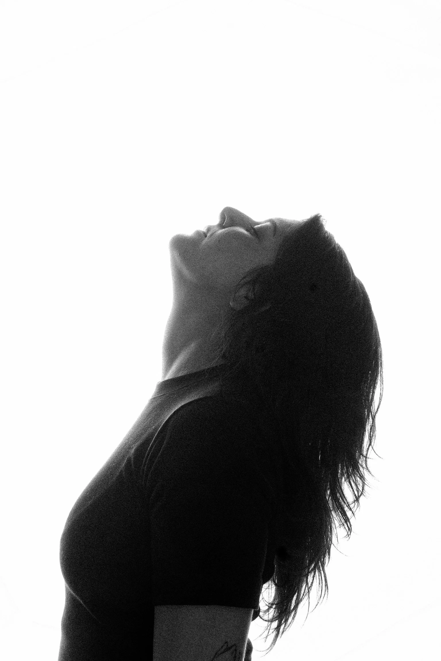 Silhouette of a woman with long hair, looking upwards, wearing a fitted short sleeve top, against a white background.