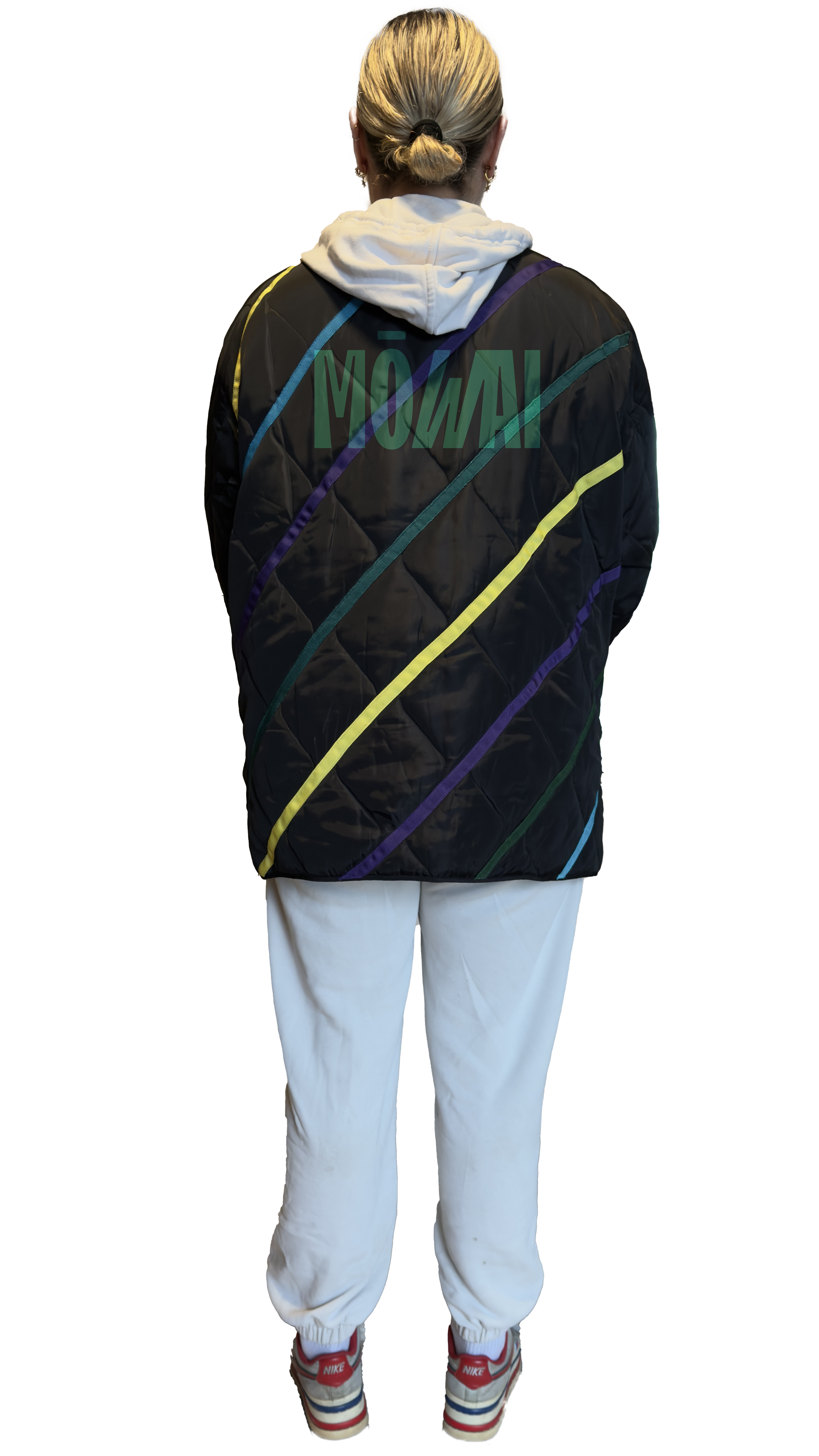 Back of a person with blonde hair tied in a bun, wearing a white hoodie, a colorful quilted jacket with diagonal lines, white sweatpants, and Nike sneakers.