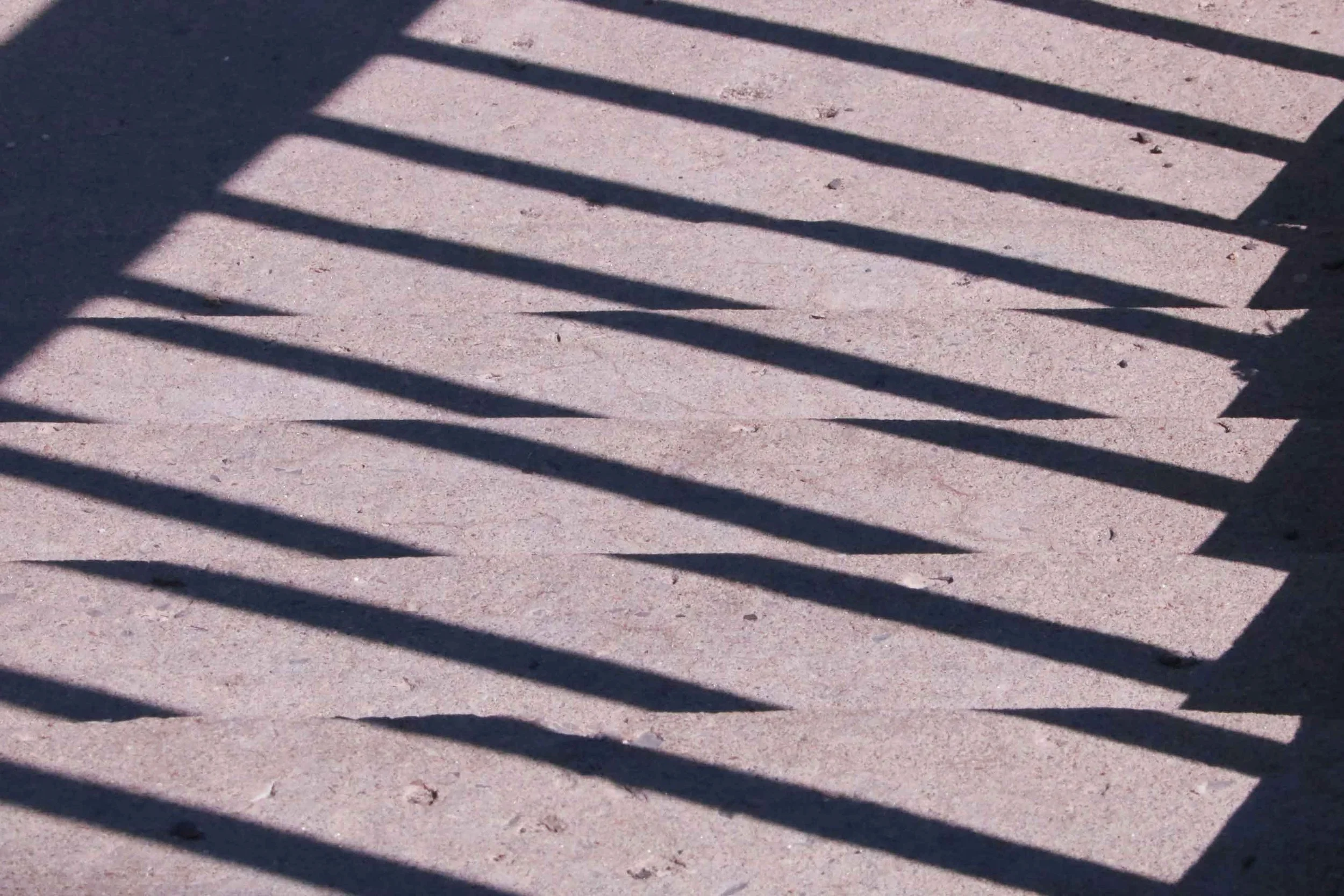 Shadows of a railing cast on a concrete sidewalk.