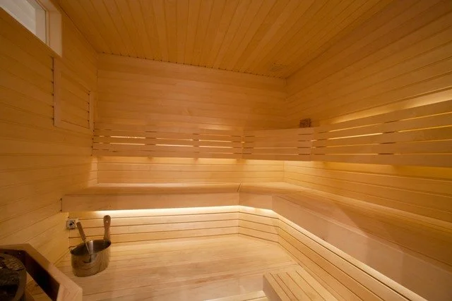 A wooden sauna with benches, a bucket, and a ladle inside.