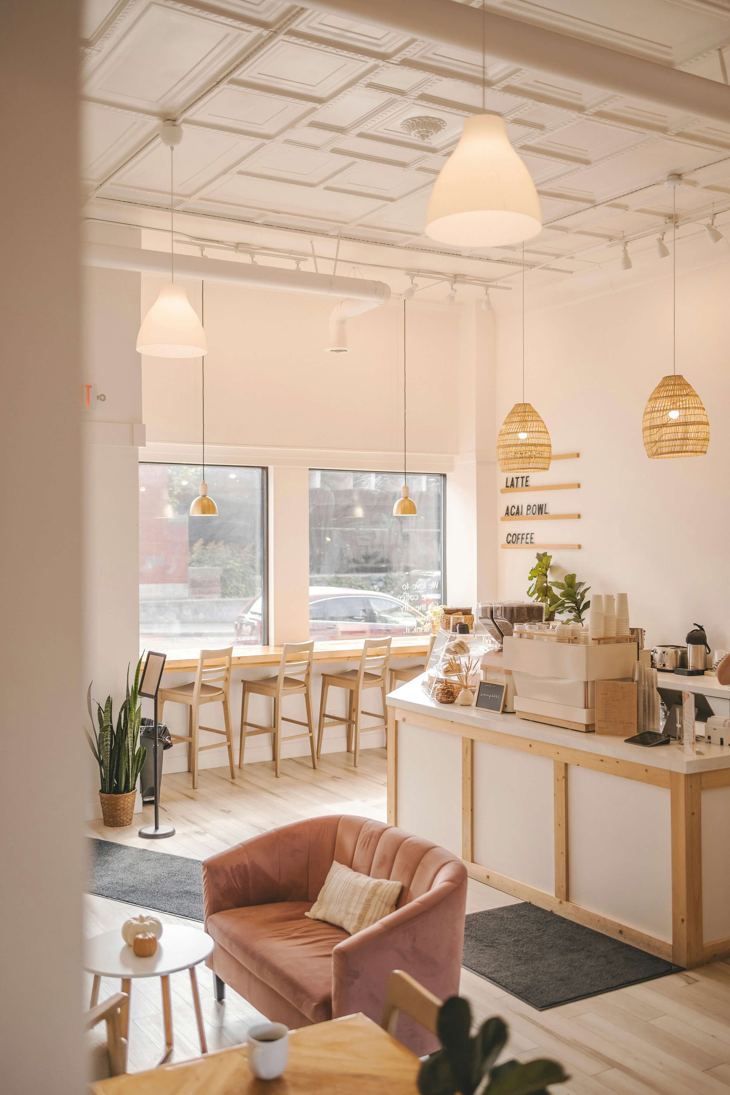 Interior of a modern coffee shop with natural light, a pink armchair, small side table, coffee counter, bar seating near the window, and minimal decor. Business consulting and development in the Hudson Valley, NY, by Shale Hill Strategies.