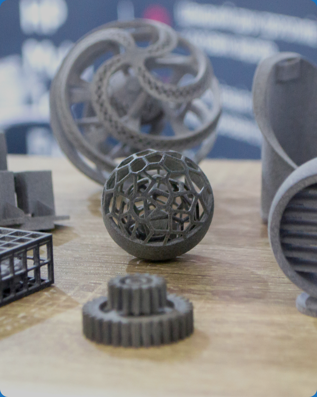 Various 3D-printed geometric objects on a wooden surface, including spheres, gears, and lattice structures.