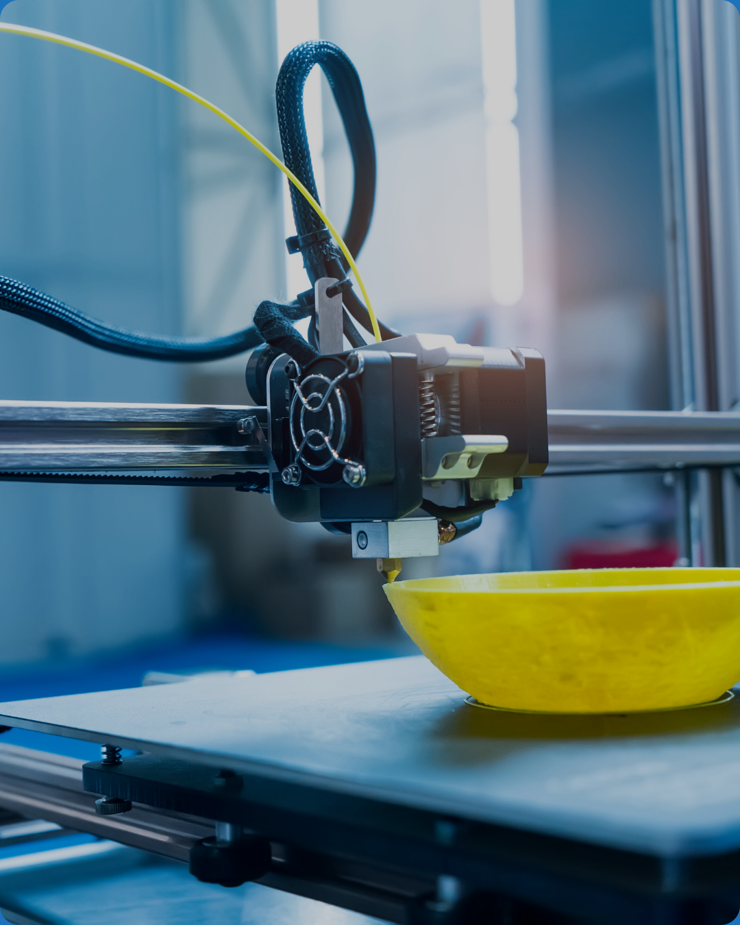 A 3D printer printing a yellow object in a manufacturing setting.