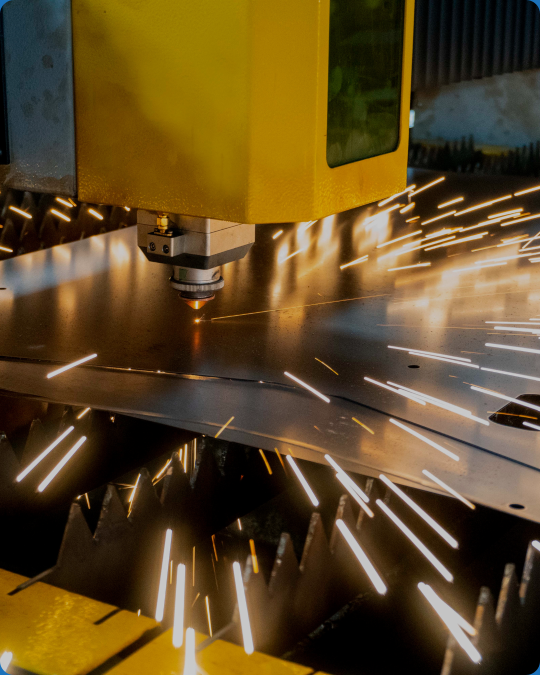 Industrial laser cutter emitting sparks as it cuts through metal sheet in a factory setting.
