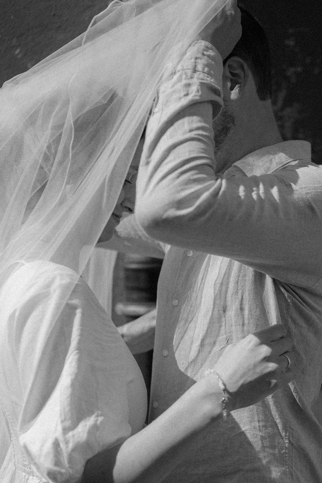 A black and white photograph of a couple sharing an intimate moment, with the woman wearing a veil and the man in a button-up shirt, their foreheads touching.