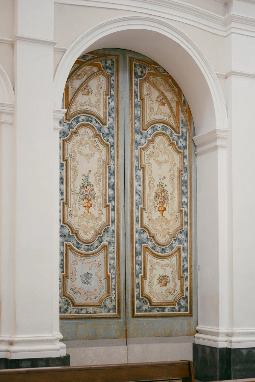Ornate double doors with floral and decorative patterns, set within a white arched doorway.