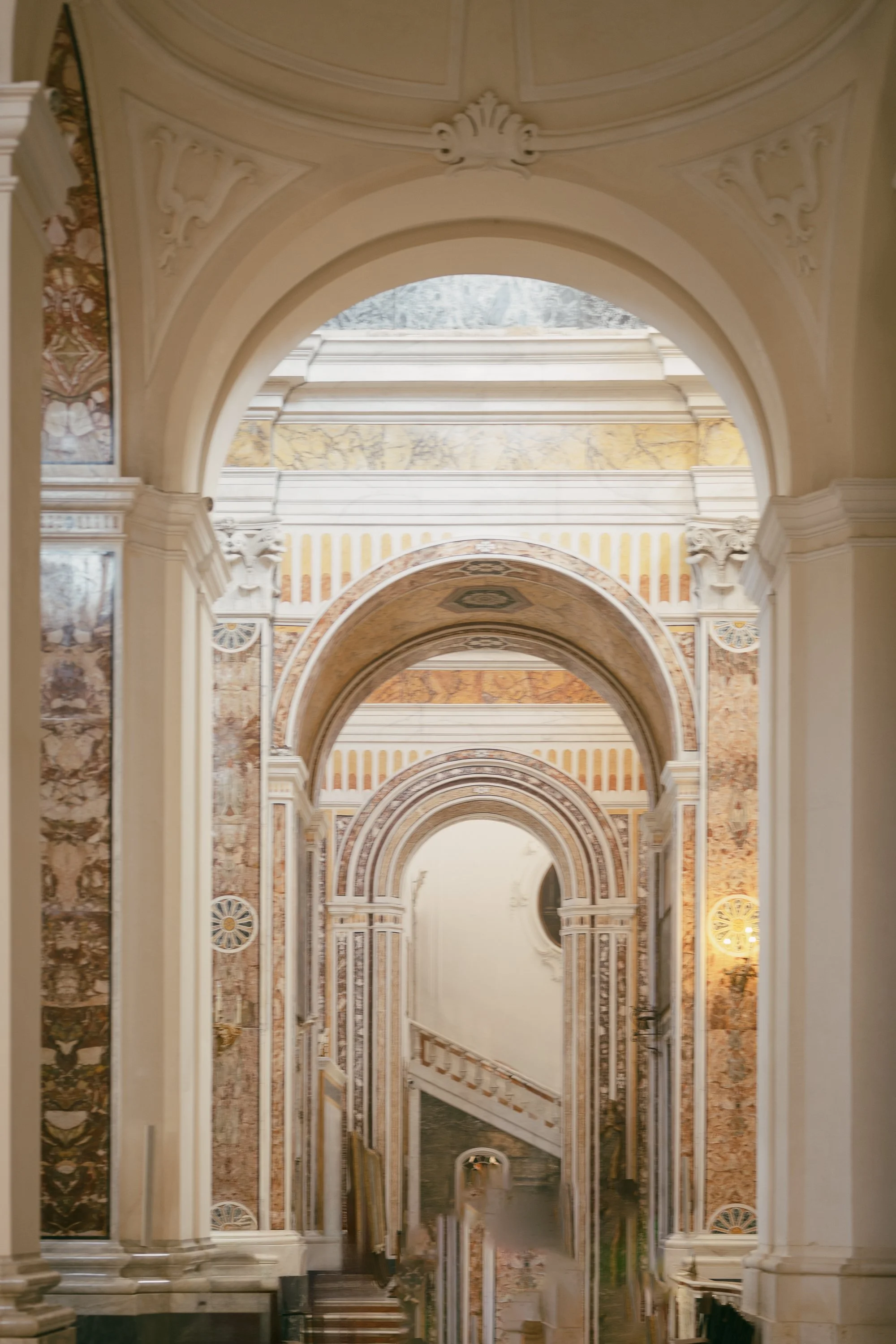 View of ornate marble arches and decorative walls inside a grand building, with a staircase at the bottom.