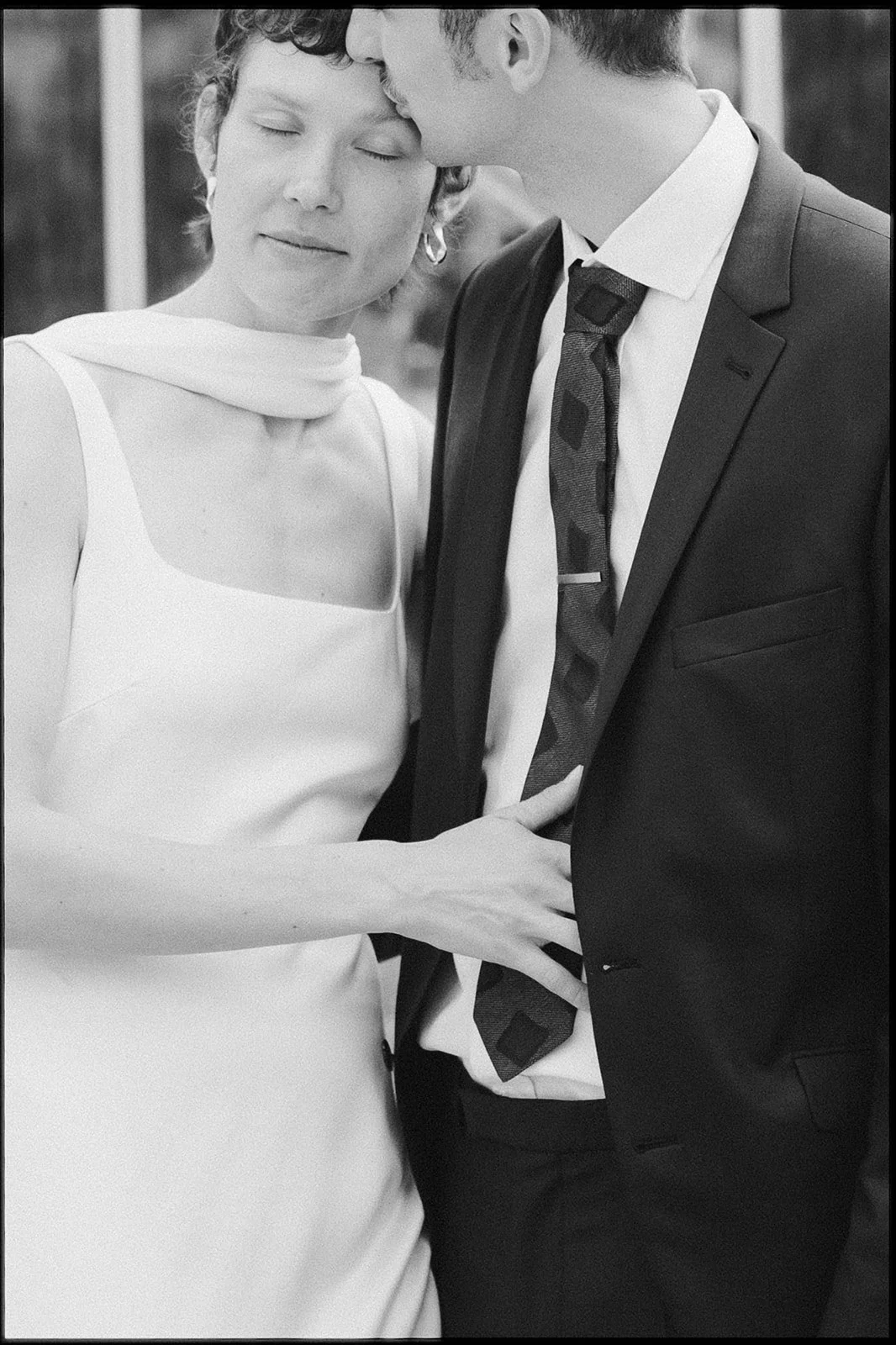 A black-and-white photograph of a couple, where the woman gently holds the man's waist and they are sharing a tender moment, with the woman closing her eyes and the man leaning in.
