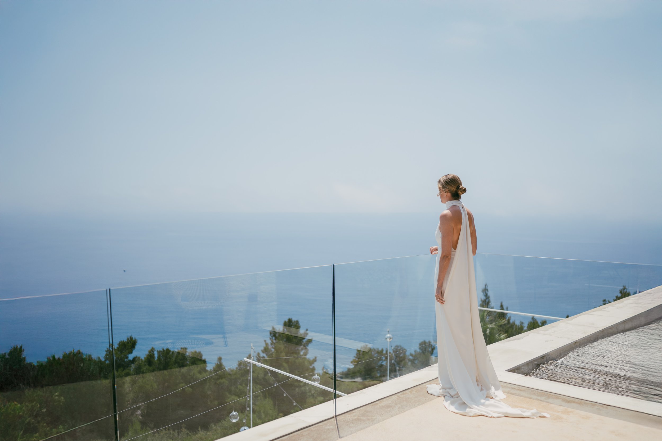 A woman in a white dress standing on a balcony overlooking the ocean.
