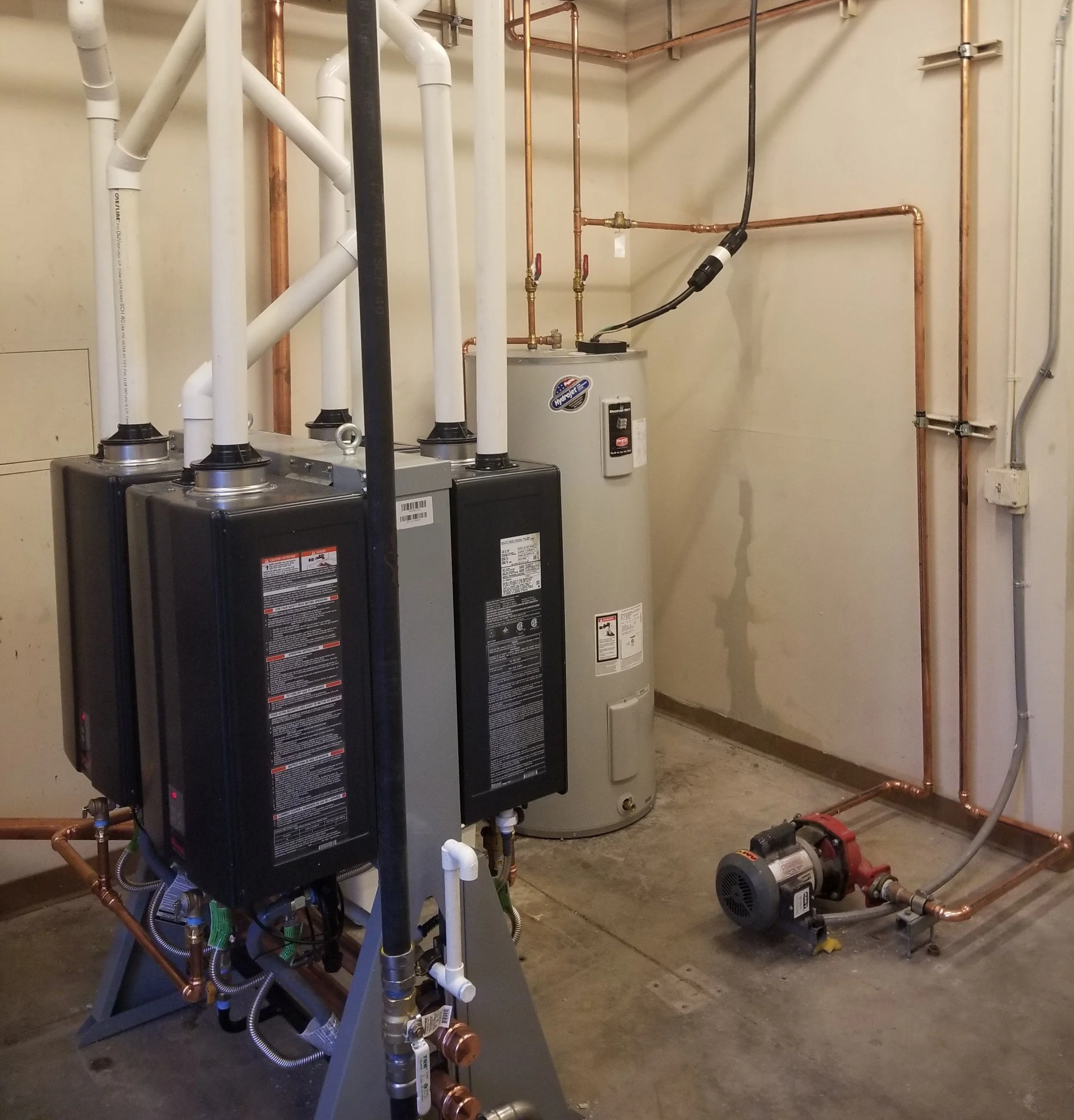A utility room with water heater, water softener, and plumbing pipes.
