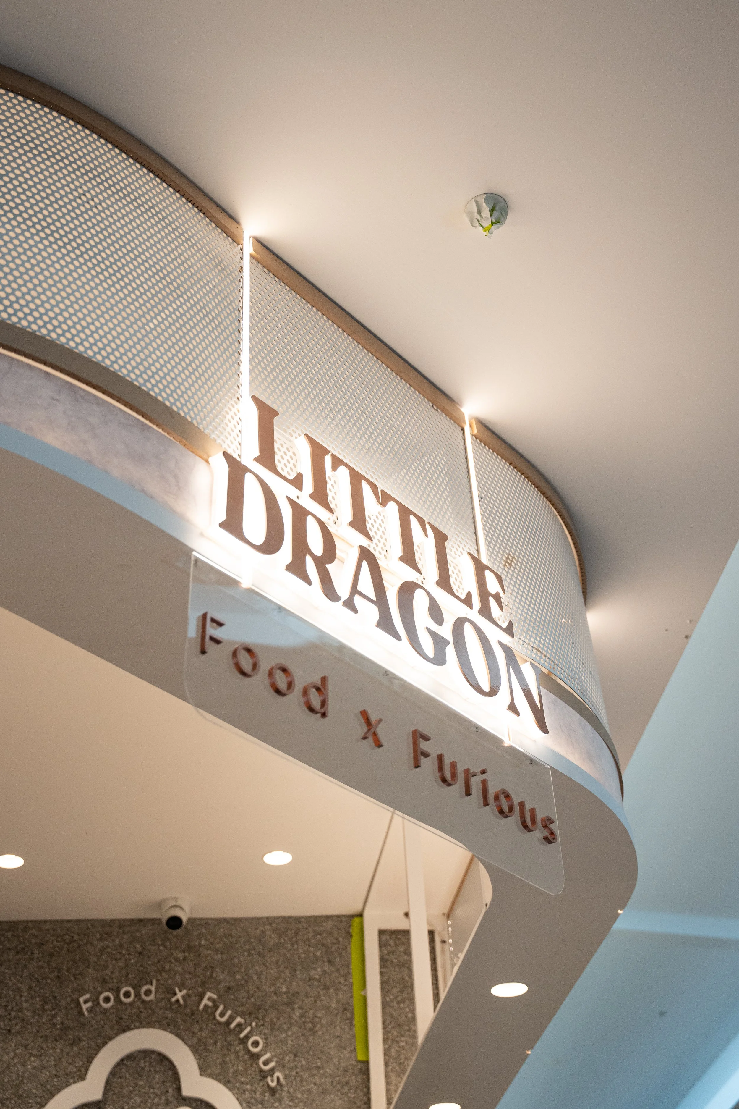 Sign displaying 'Little Dragon' with a tagline 'Food x Furious' underneath at a food court or mall.