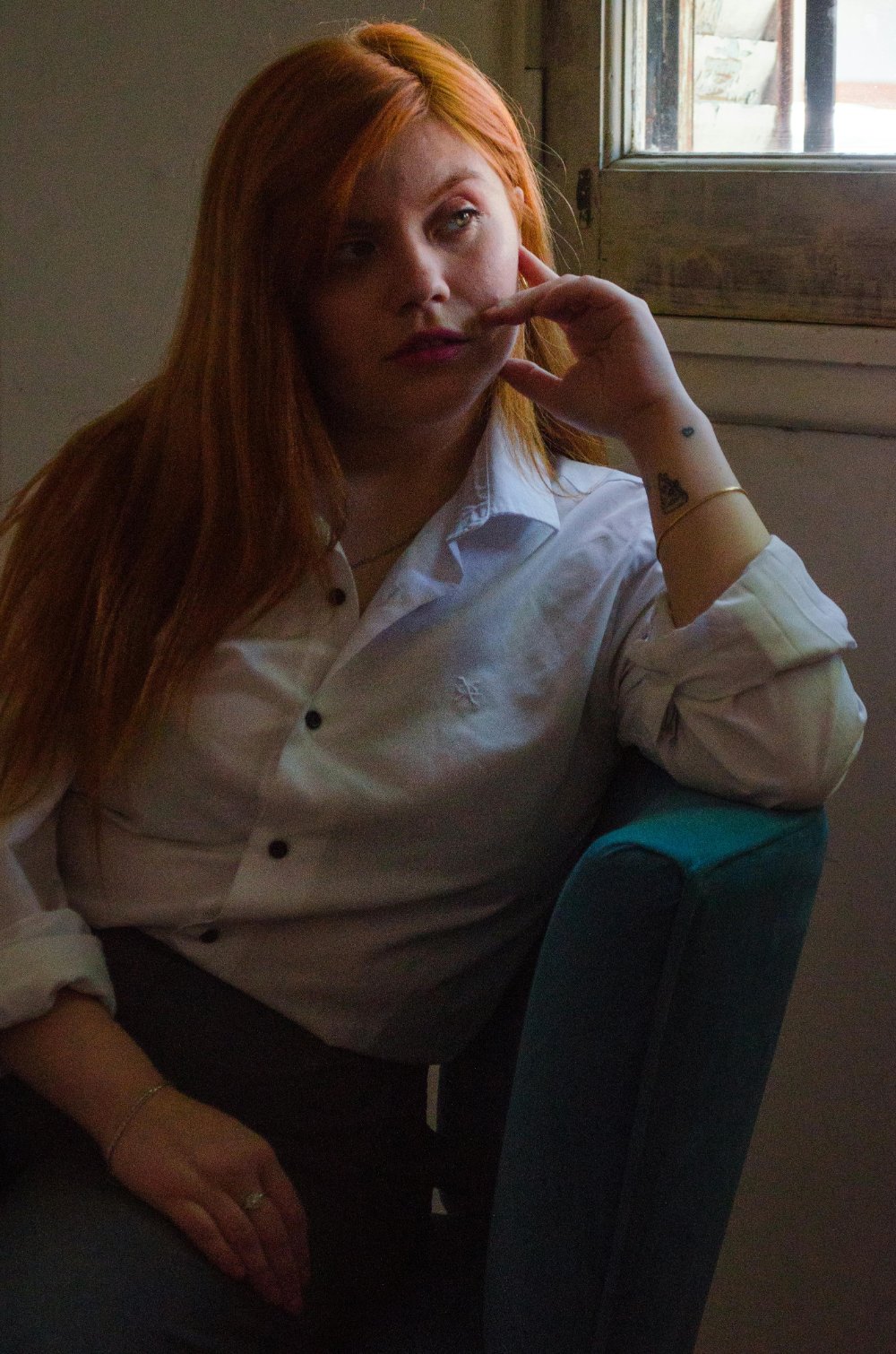 Woman sitting indoors by a window, looking thoughtful and reflective. | EMDR therapy NYC