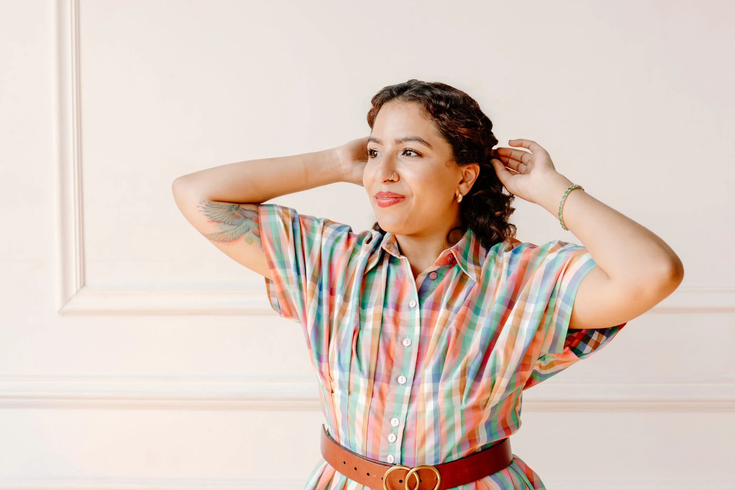 EMDR and DBR therapist Jennifer Budhan standing in a bright, welcoming office, smiling warmly adjusting her hair.