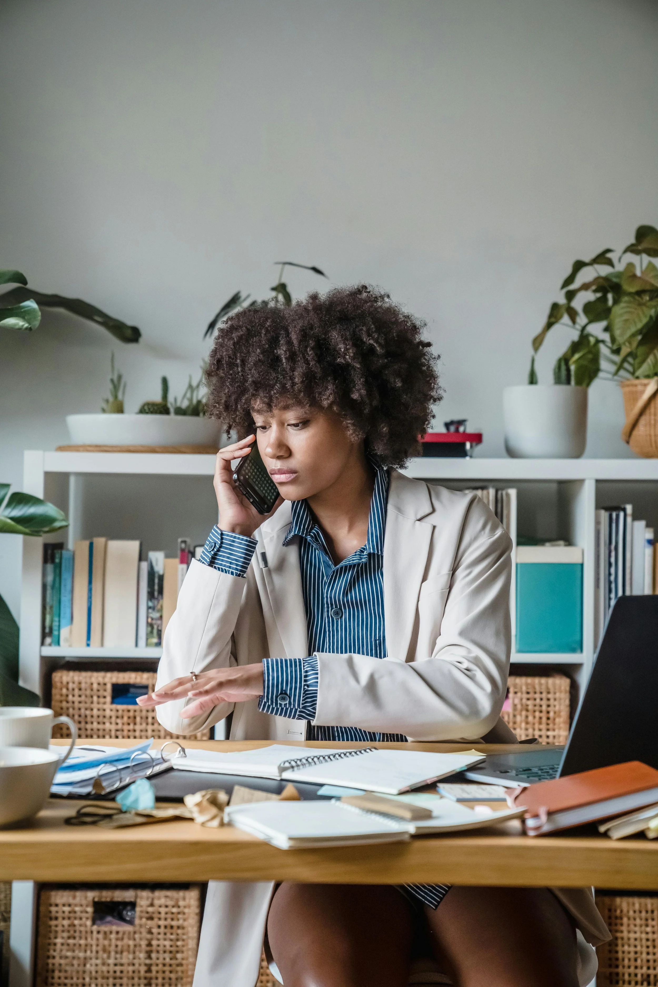 Woman working at a desk while talking on the phone, juggling papers and tasks, illustrating emotional labor and holding everything together.