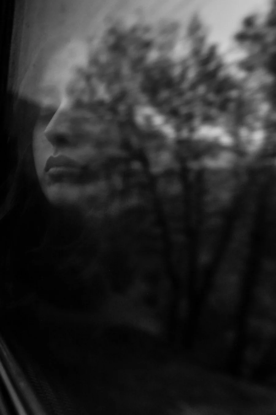 A blurred reflection of a woman in a window, showing the quiet, somber moments when the inner critic clouds clarity and self-trust.