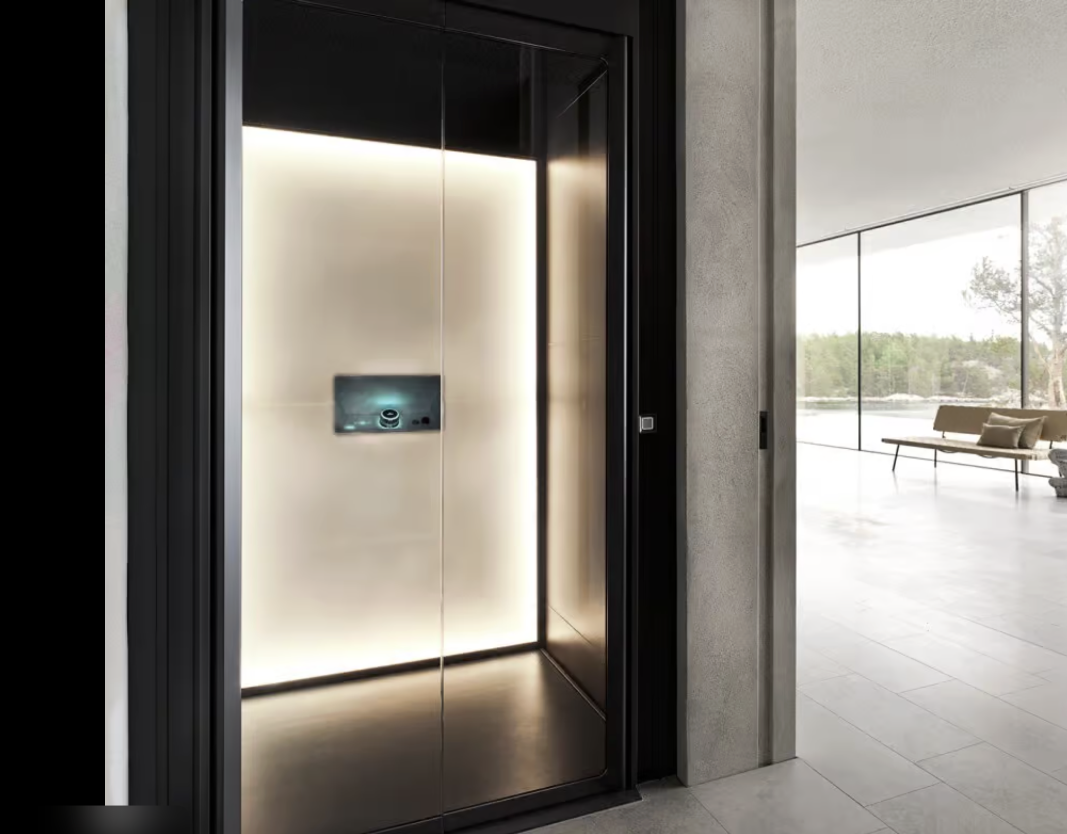 Modern glass elevator with illuminated interior, next to a bright and spacious room with large windows and a seating area.