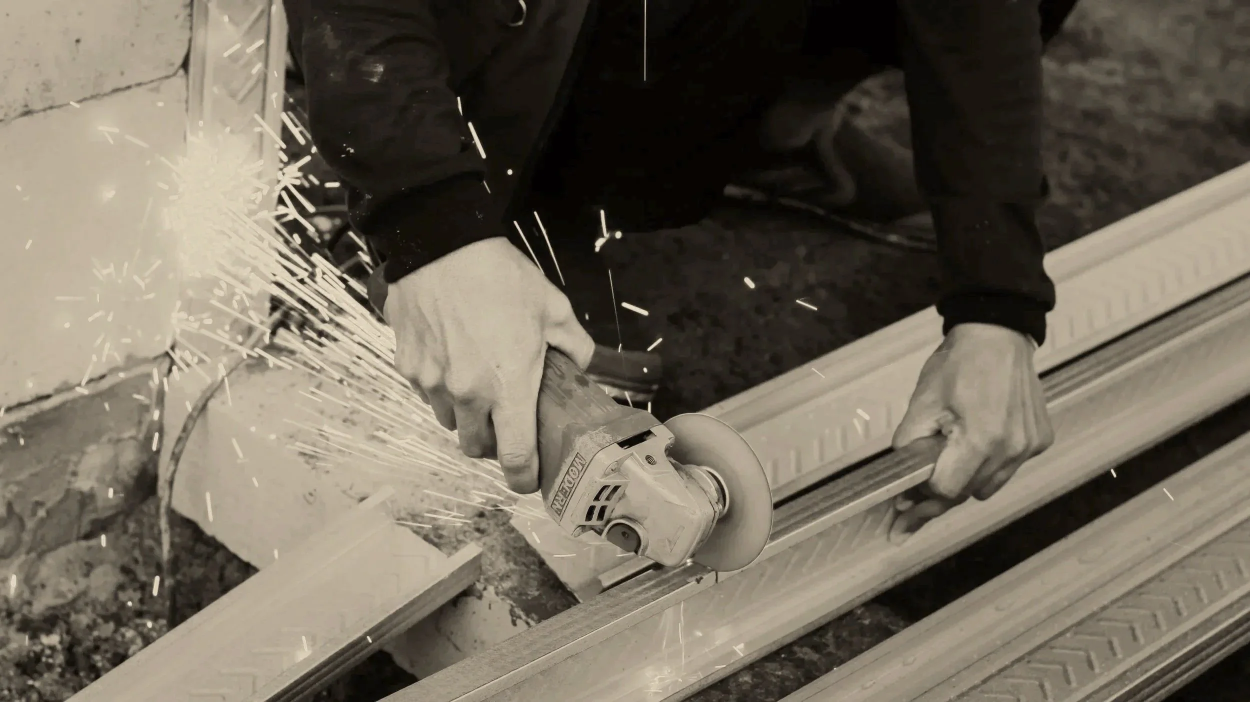 Person wearing gloves using an angle grinder to cut a wooden board, with sparks flying.