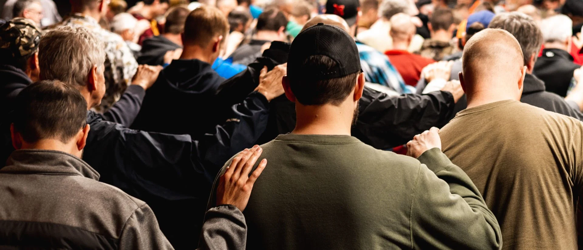 A group of people standing close together with arms around each other's shoulders in a prayer or moment of silence.