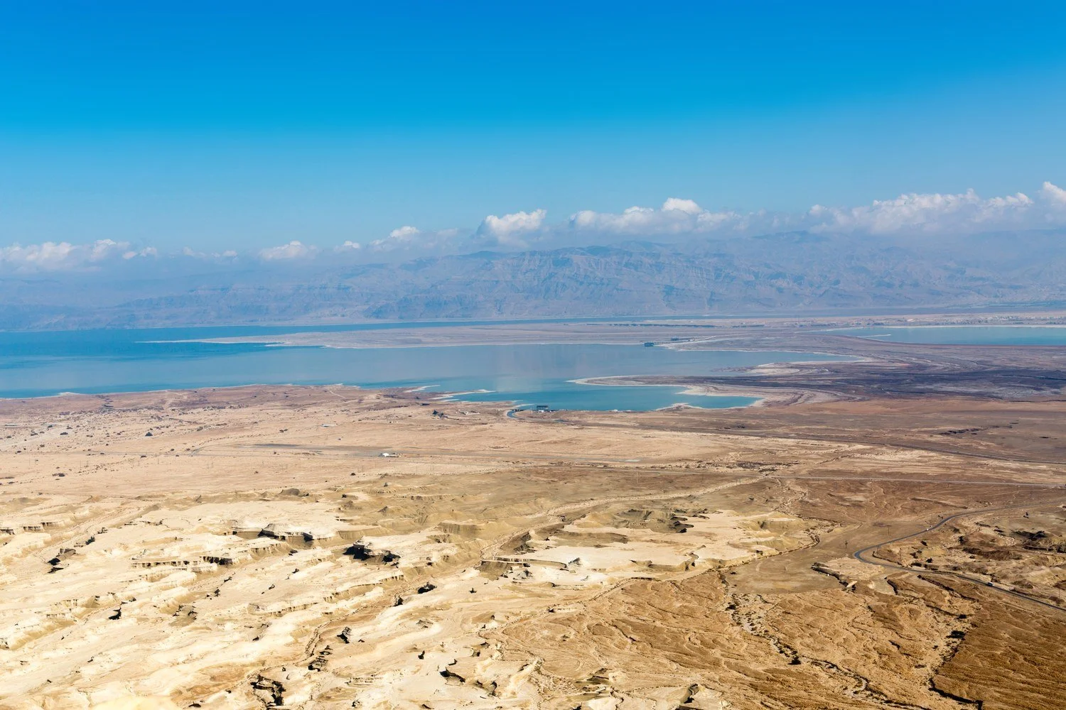 View from the top of Masada over pale eroded badlands, lagoons and salt flats with distant mountains and cloud