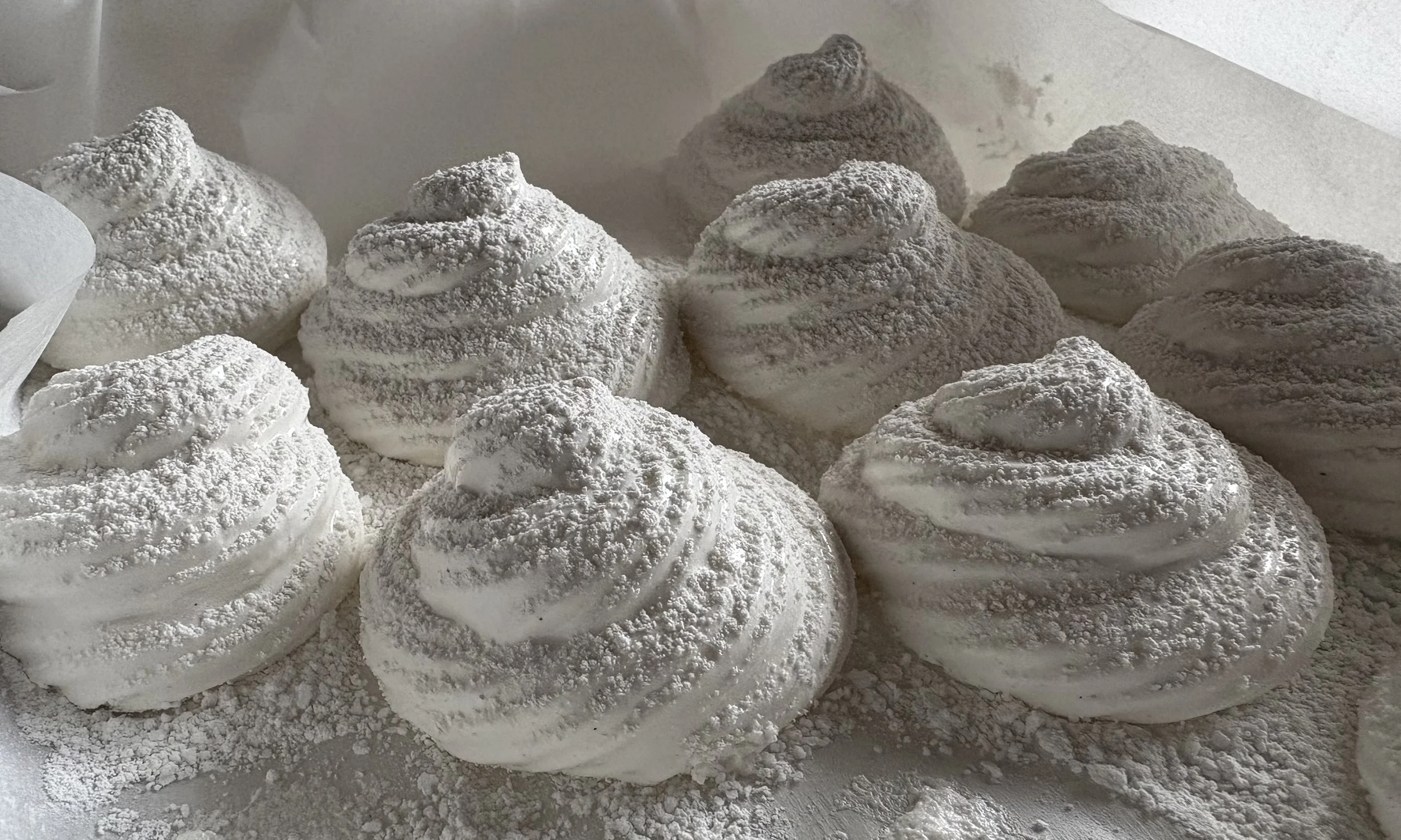 Multiple swirl-shaped white meringue marshmallows dusted with powdered sugar