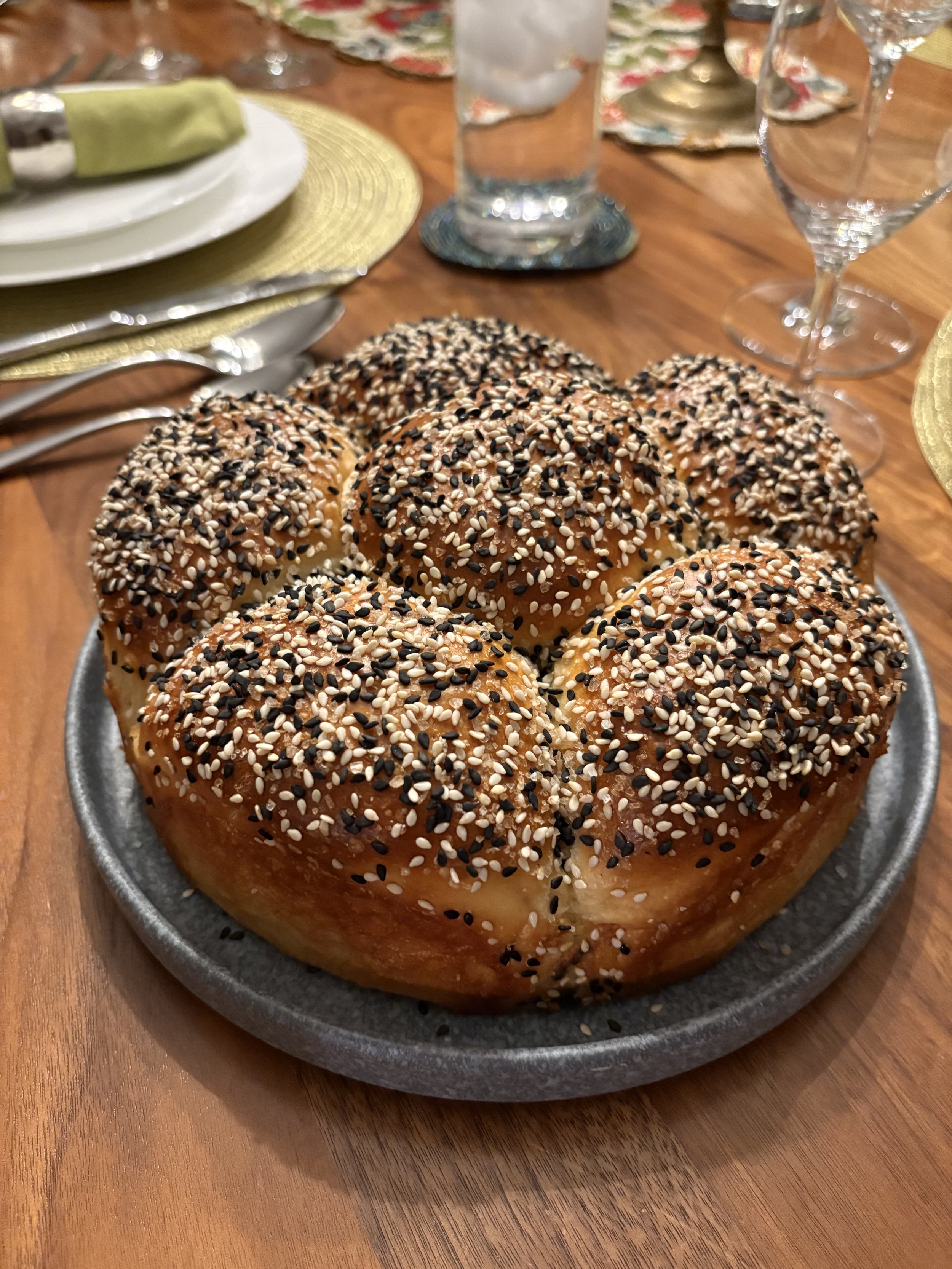 A plate of eight round bread rolls topped with sesame and black sesame seeds on a dining table set for a meal.
