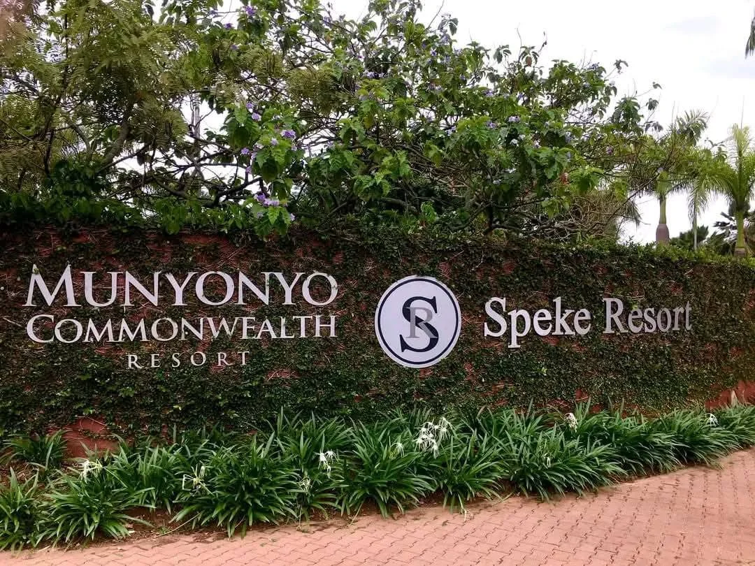 Signboard displaying the names 'Munyonyo Commonwealth Resort' and 'Speke Resort' with a decorative background of green plants and purple flowers.