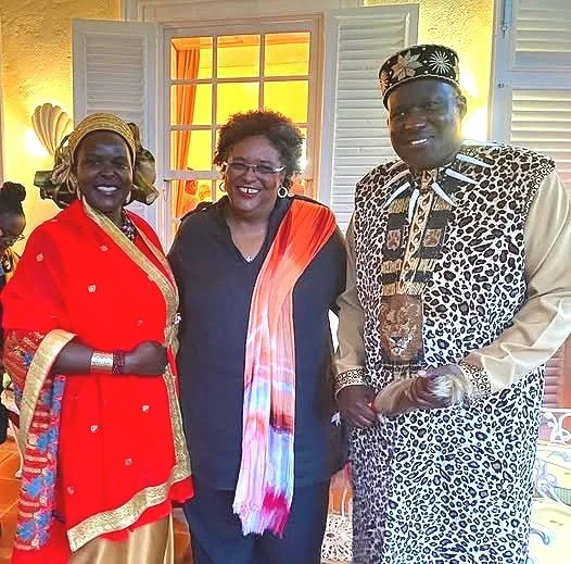Three people standing indoors, dressed in colorful traditional and modern attire, smiling for the photo.