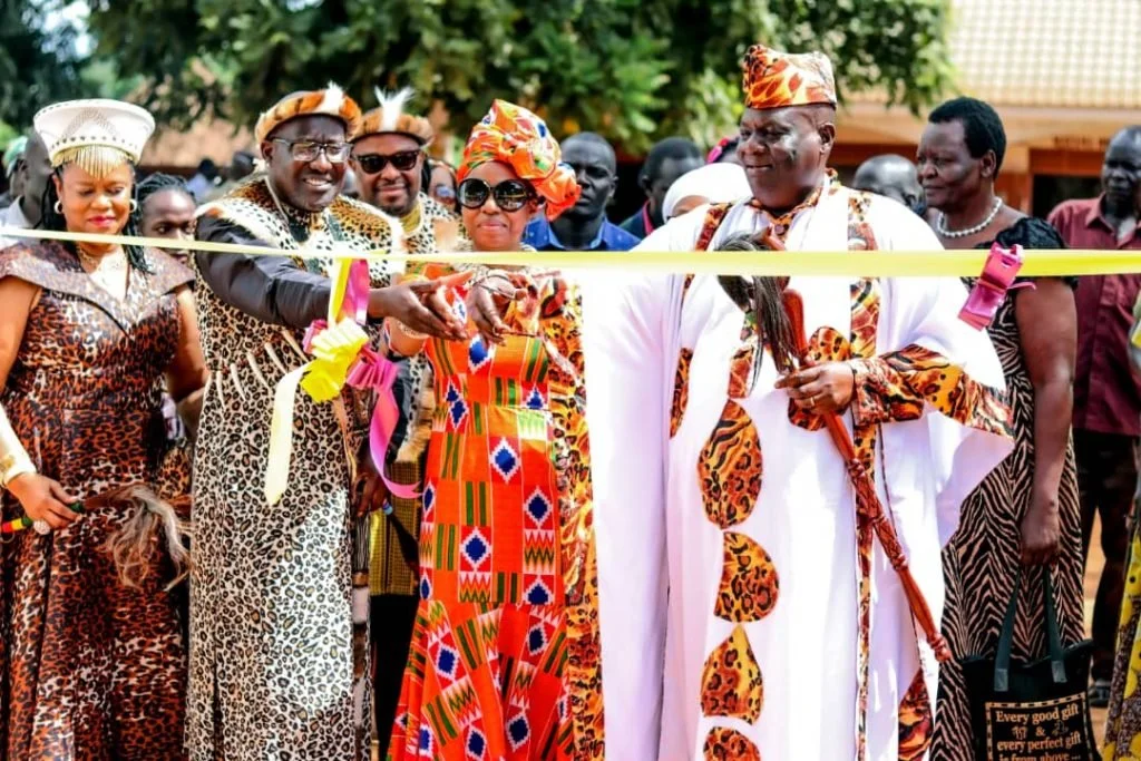 Group of people at a ribbon-cutting ceremony, dressed in colorful traditional African attire, outdoors with trees in the background.