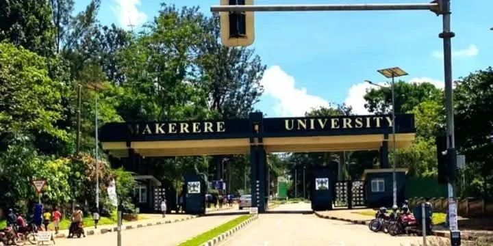 Entrance gate of Makerere University with trees, vehicles, and pedestrians around.