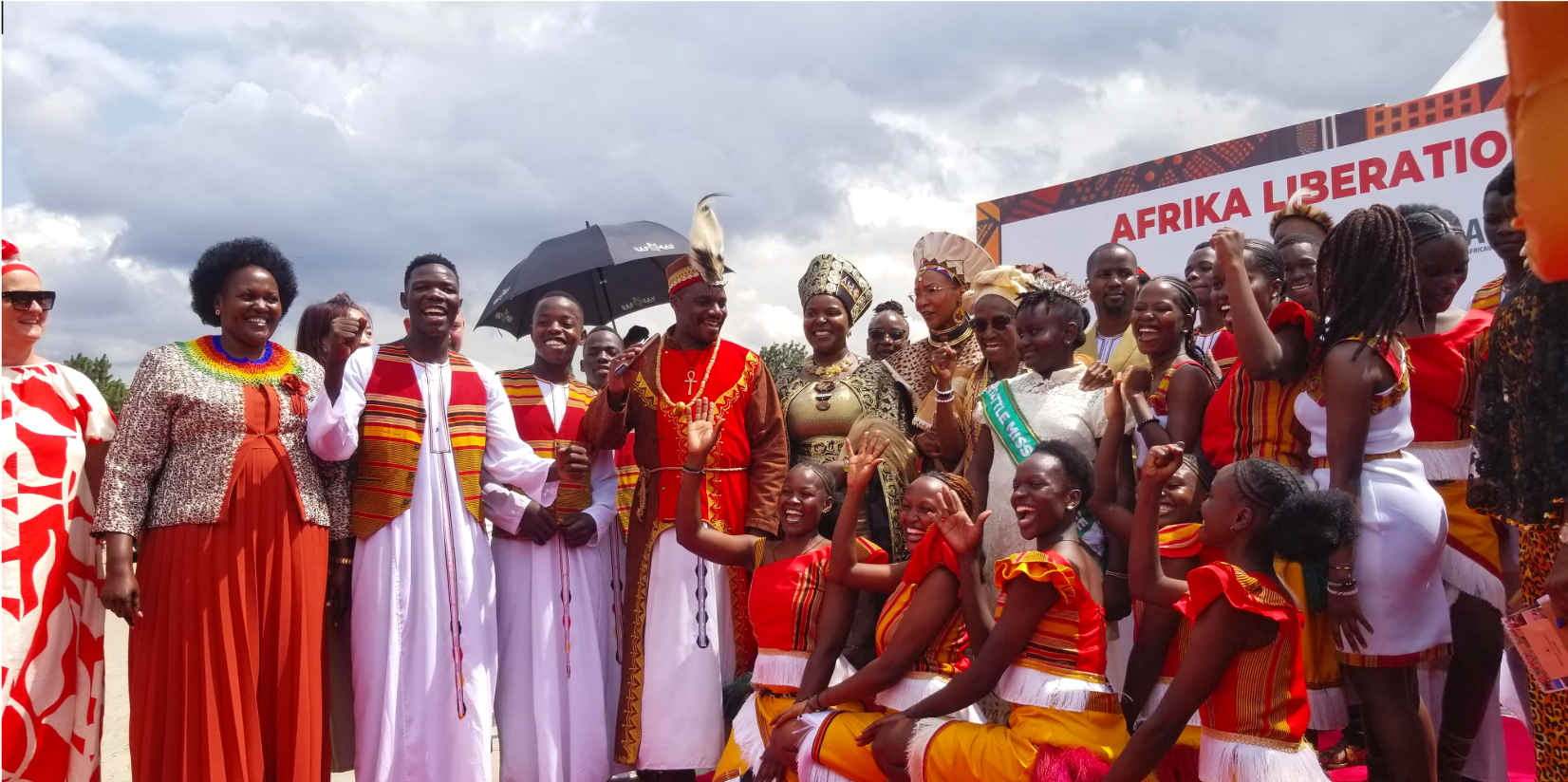 Group of people dressed in traditional African clothing celebrating outdoors under cloudy sky.