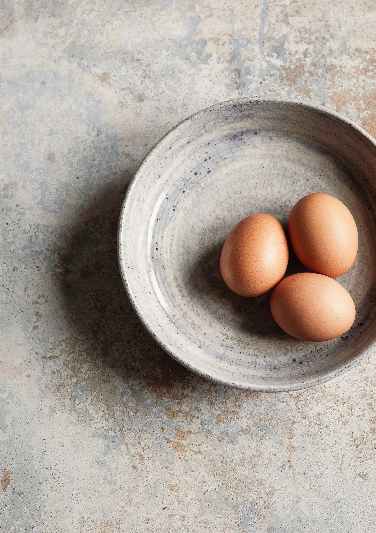 Three brown eggs in a ceramic bowl on a textured surface.