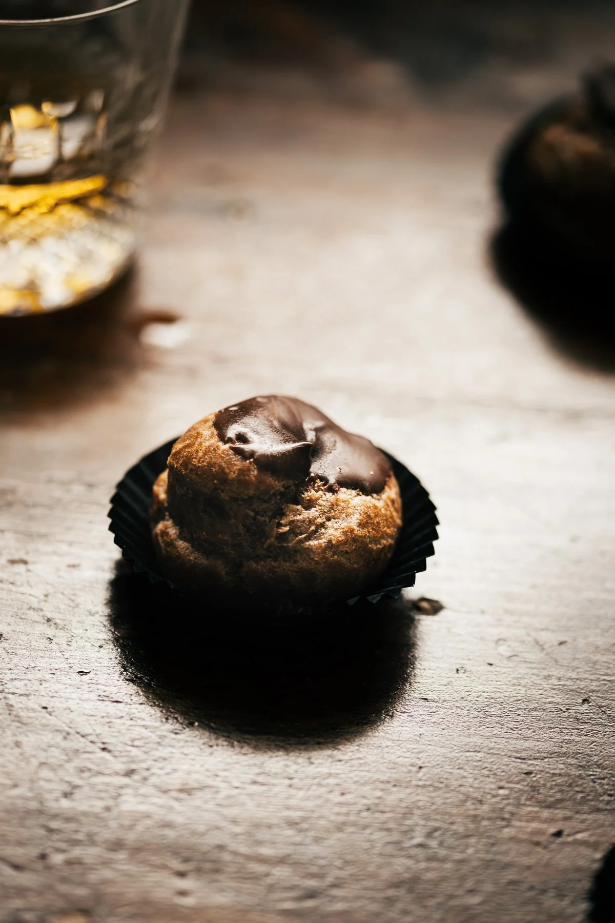 A chocolate-dipped cookie placed on a dark wooden surface with a blurred glass container in the background.