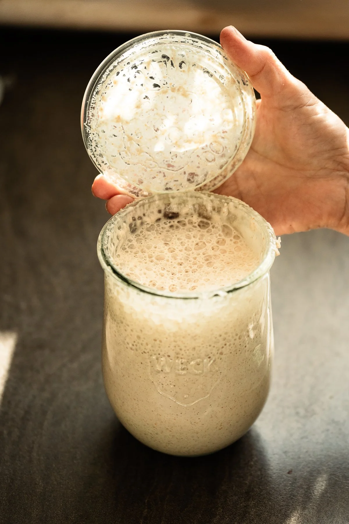 Person holding a glass jar with a liquid that appears to be milk and bubbles on the surface.