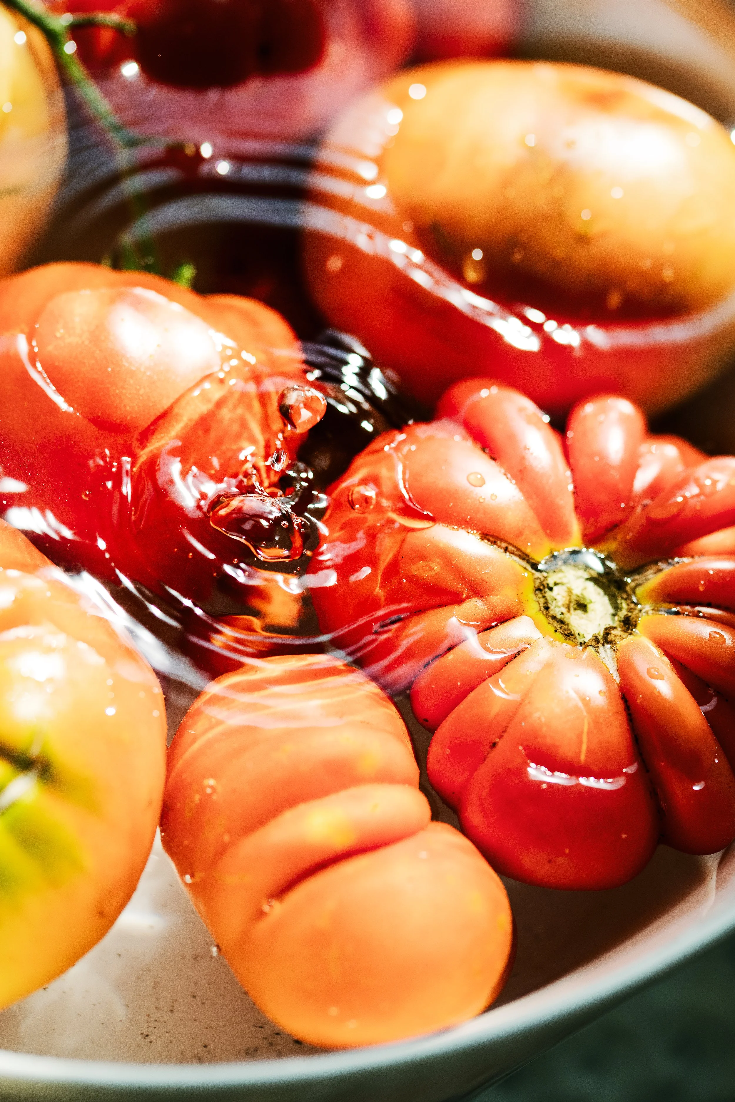 Close-up of sliced tomatoes submerged in water in a white bowl, with some whole tomatoes in the background.