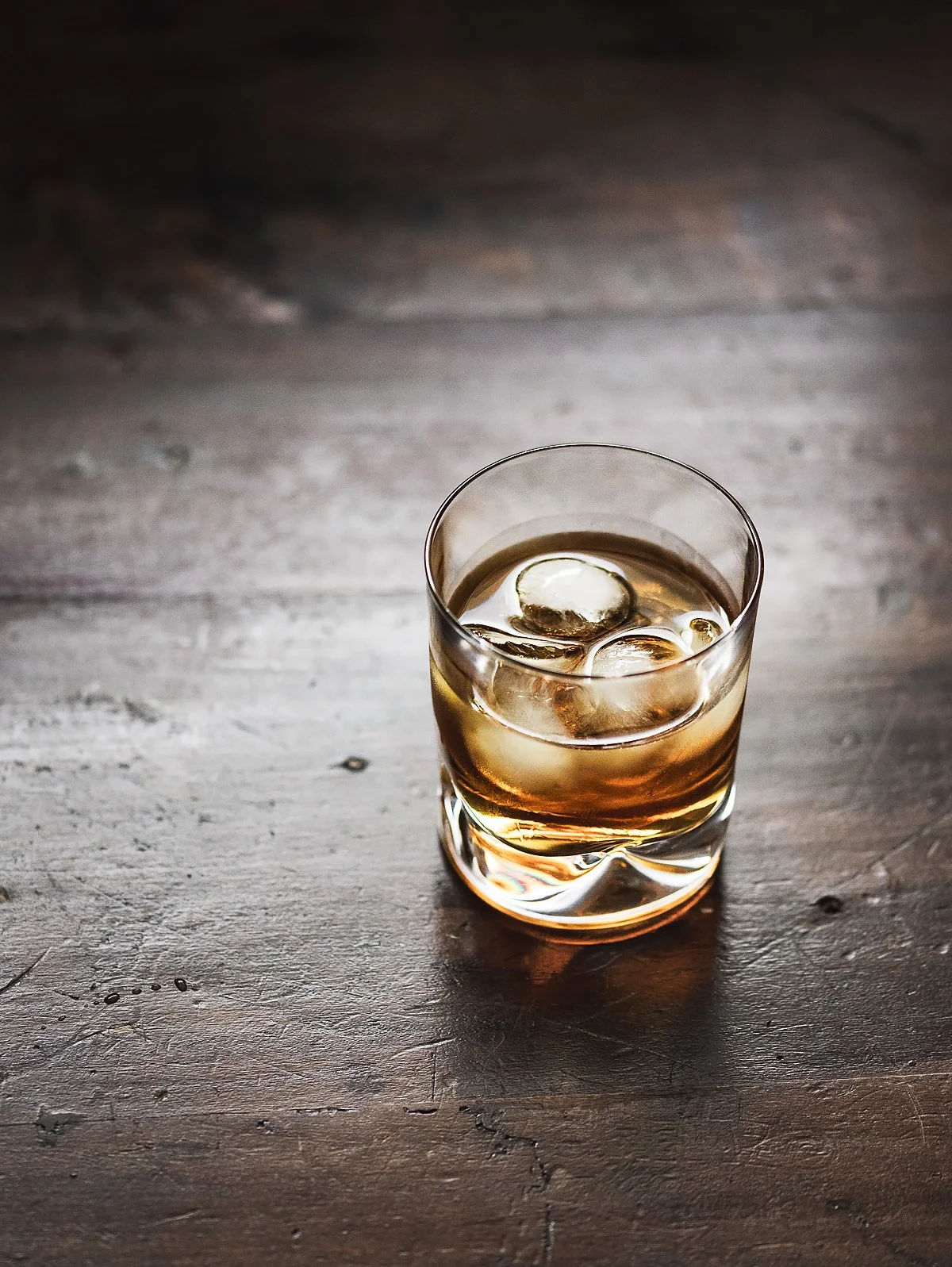 A glass of whiskey with ice cubes on a wooden surface.