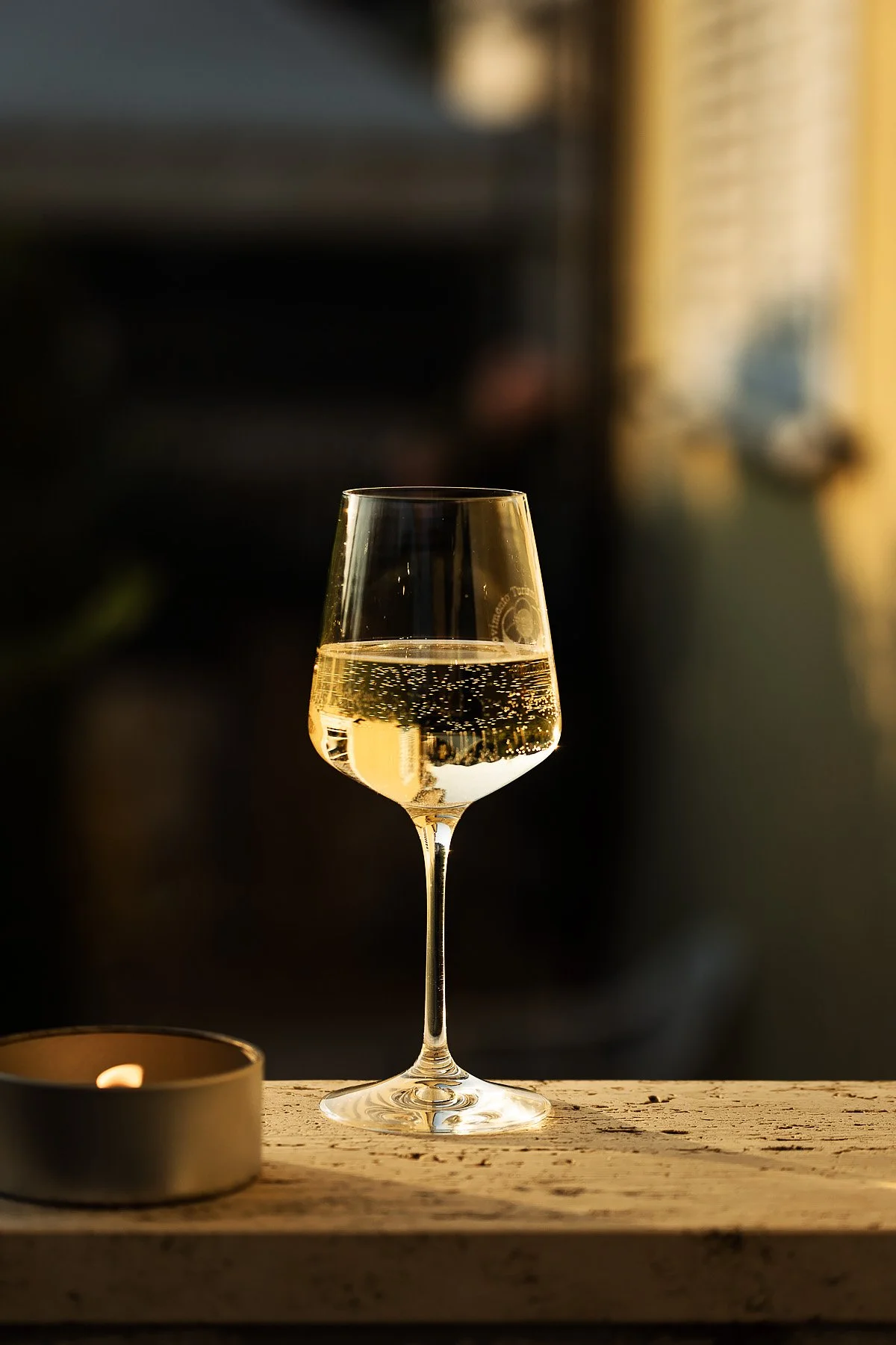 A glass of white wine on a wooden surface next to a lit candle.
