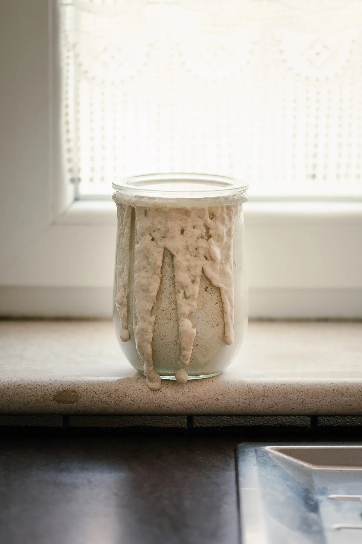 A glass jar with a candle inside, the candle's melted wax has overflowed and dripped down the sides of the jar.