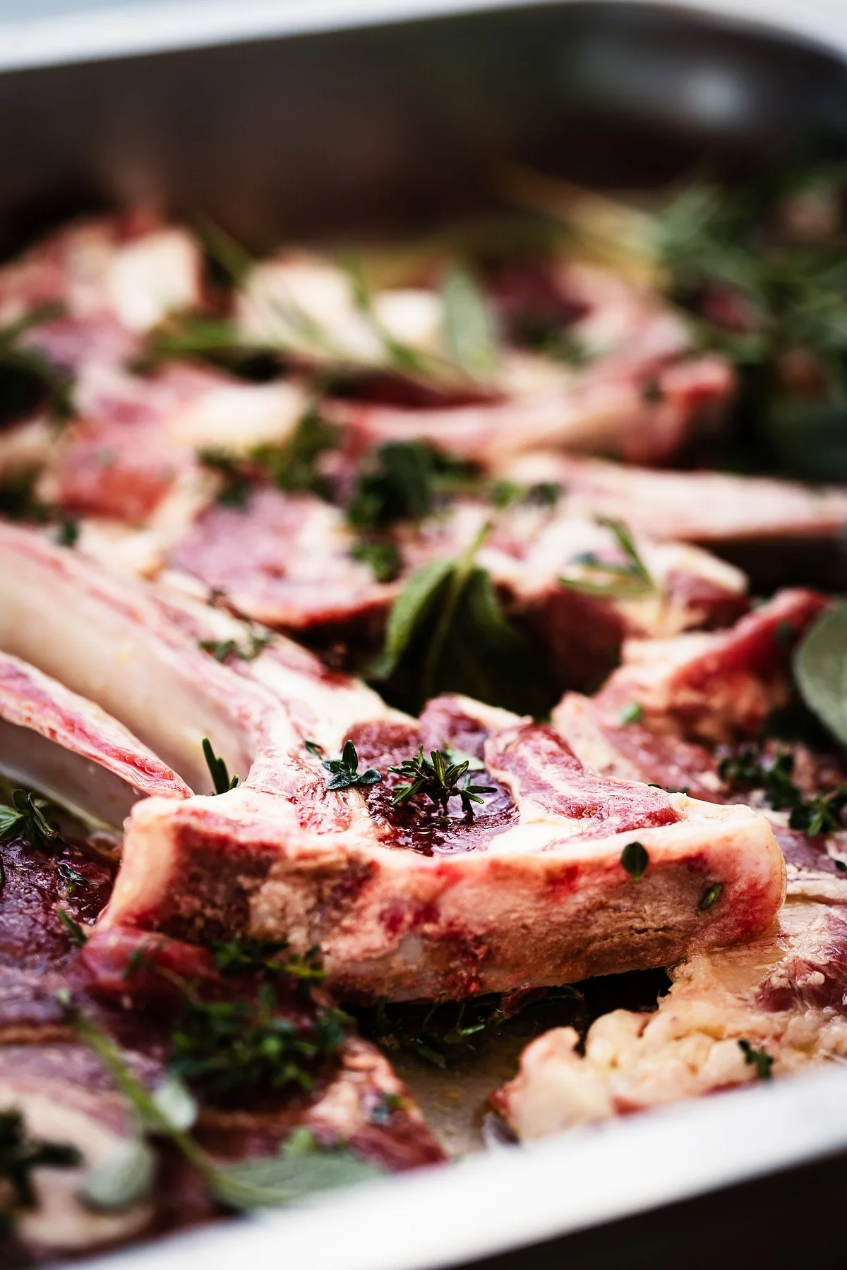 Raw lamb chops garnished with fresh herbs.