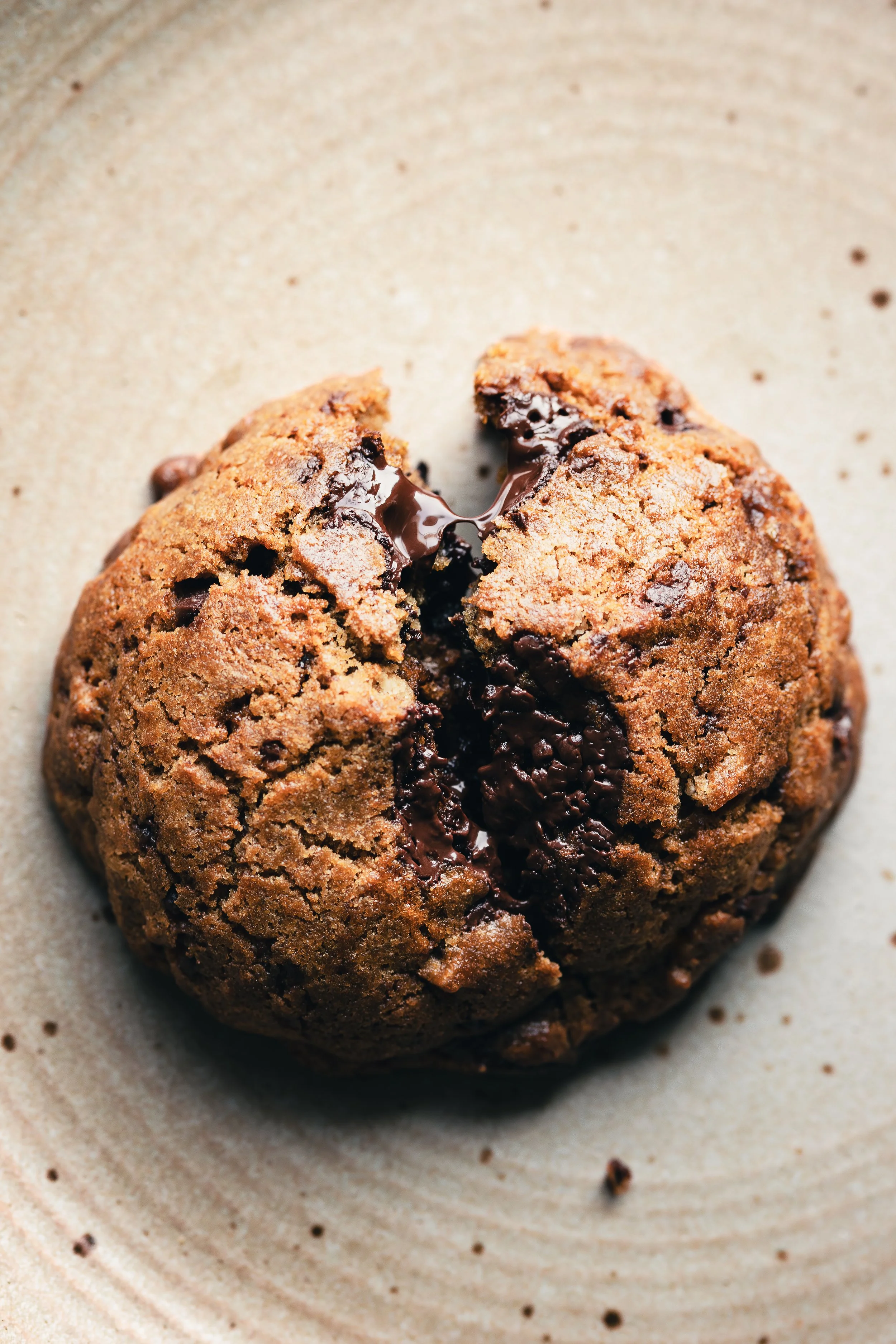 Close-up of a chocolate chip cookie with melted chocolate inside, placed on a beige plate.
