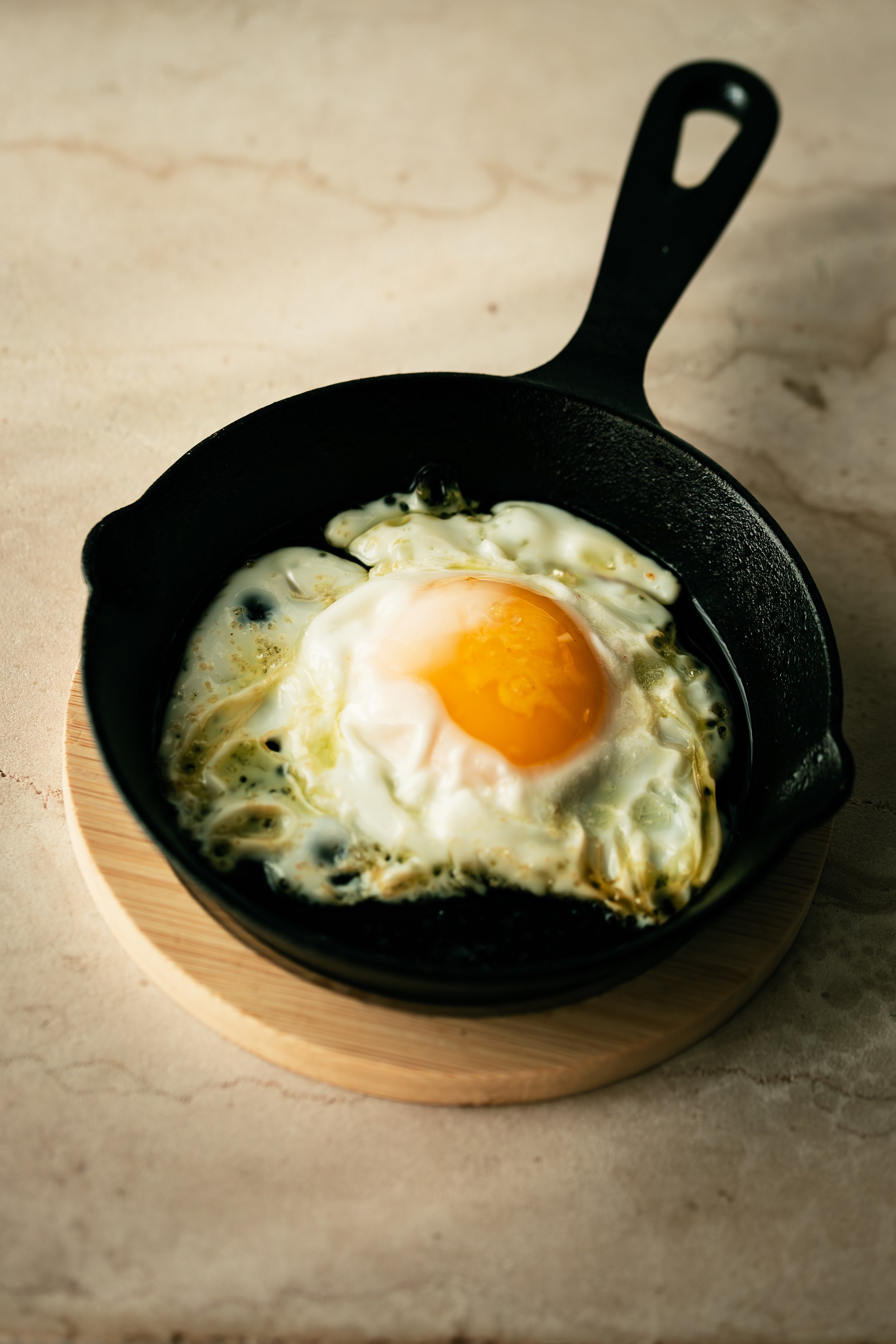 Cast-iron skillet with a fried egg, placed on a round wooden tray.