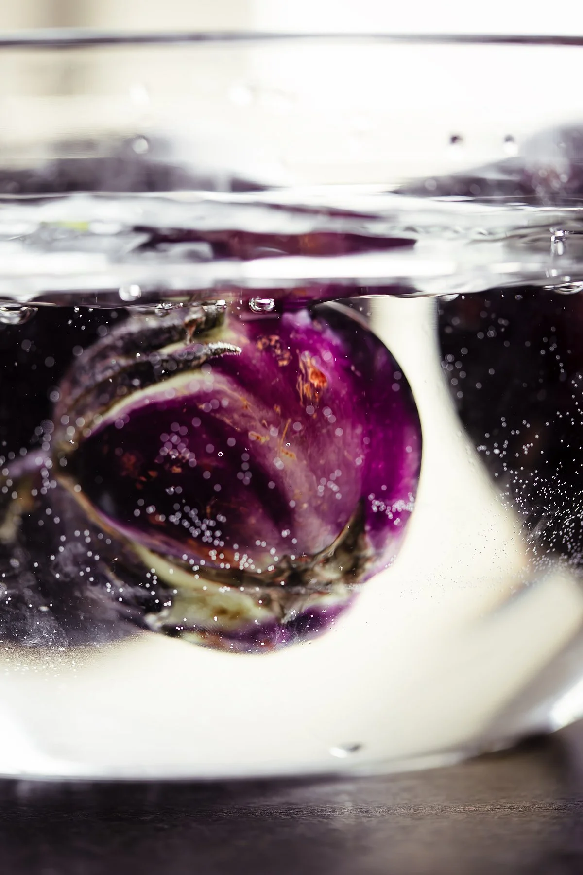 Purple eggplant submerged in water with bubbles and ripples.