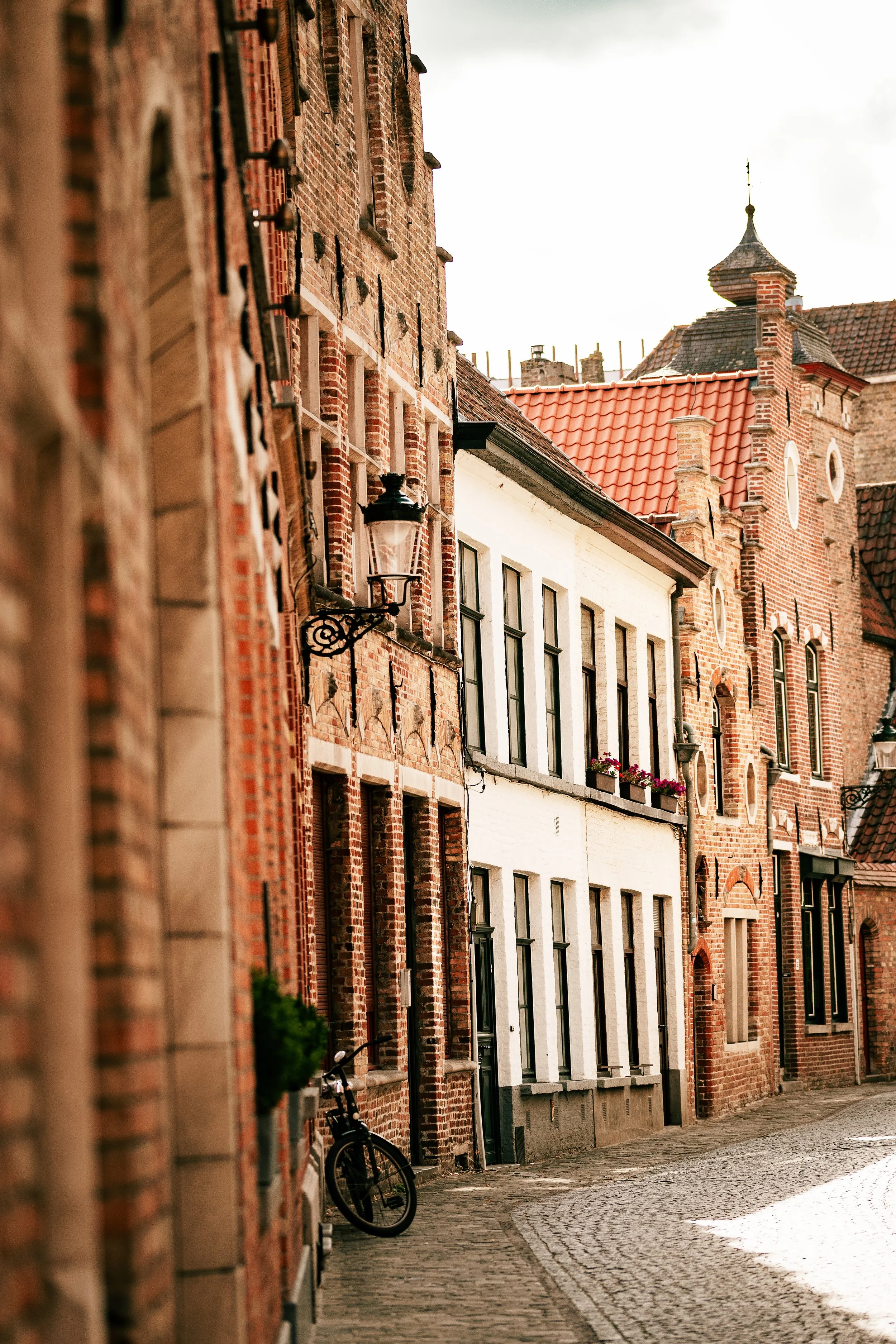 A narrow cobblestone street lined with historic brick buildings, some with flower boxes and a bicycle leaning against the wall.