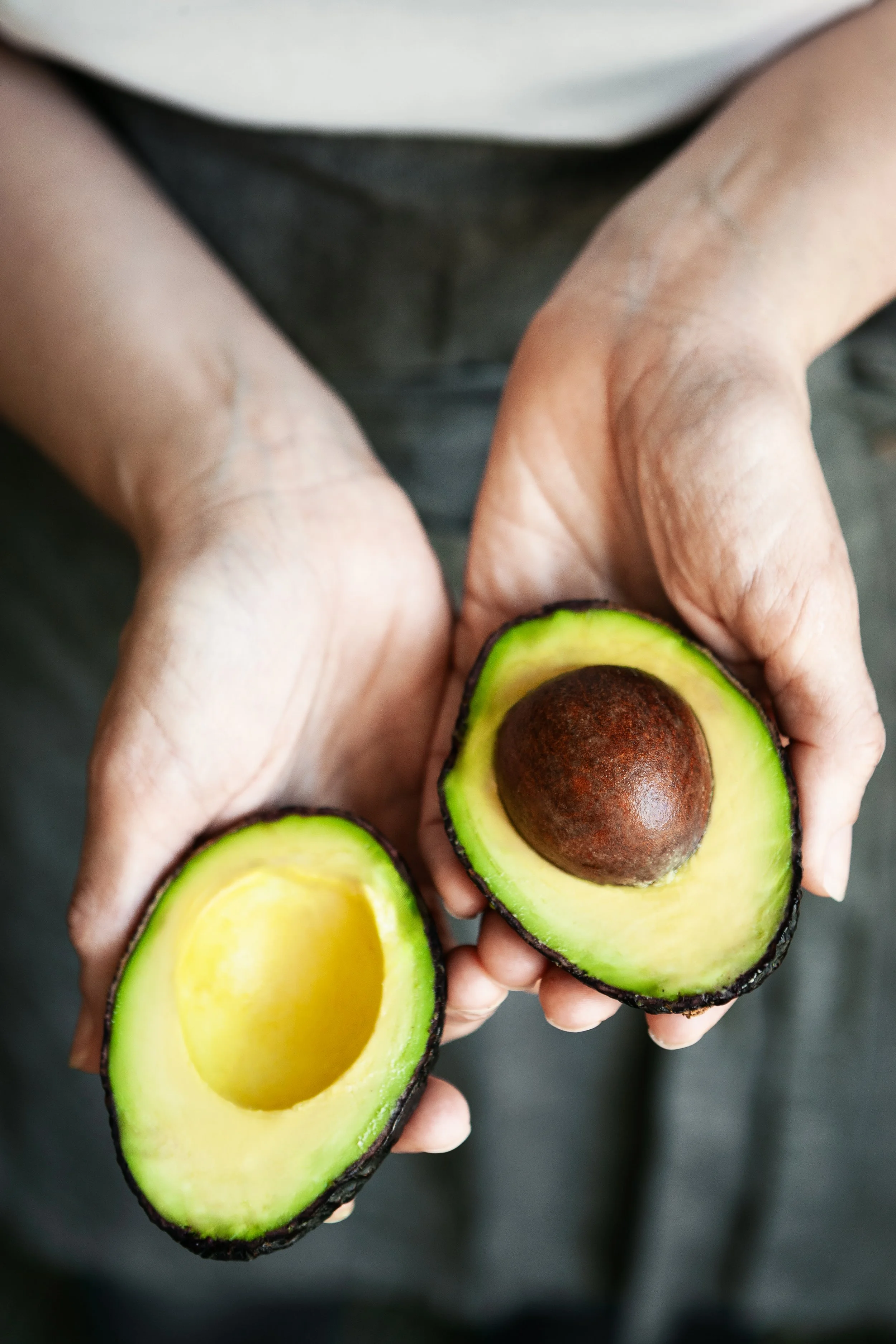 Close-up of a person holding an avocado cut in half, showing the seed and bright green flesh.