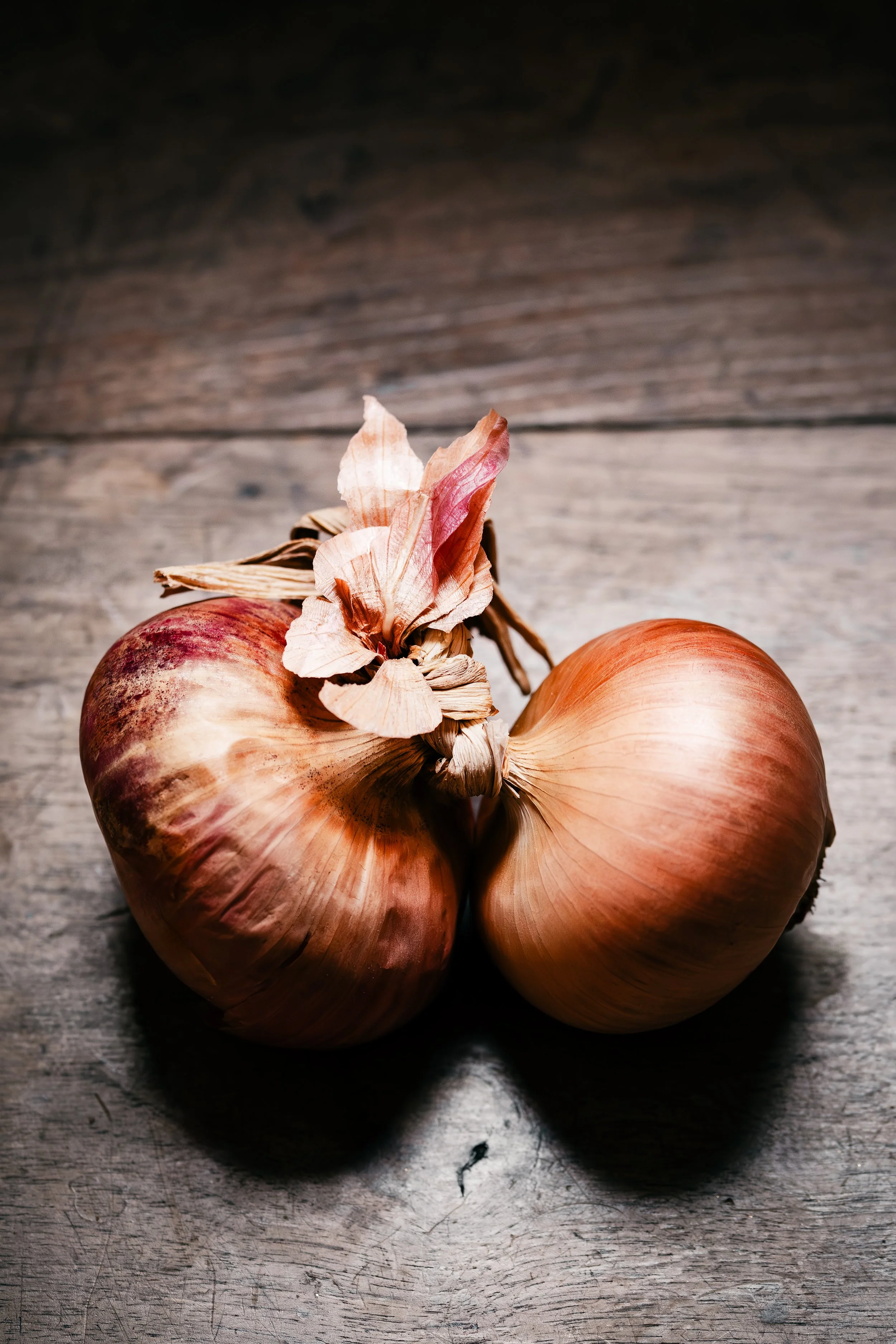 Two onions with papery skins resting on a wooden surface.