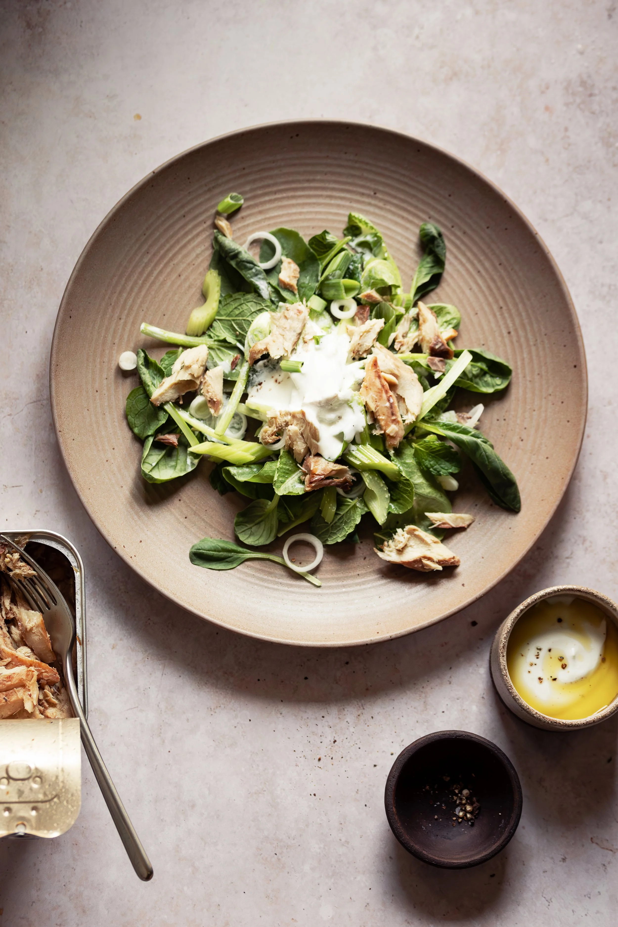 A beige bowl containing a fresh green salad with chopped chicken, sliced green onions, and a poached egg on top, on a light-colored countertop.