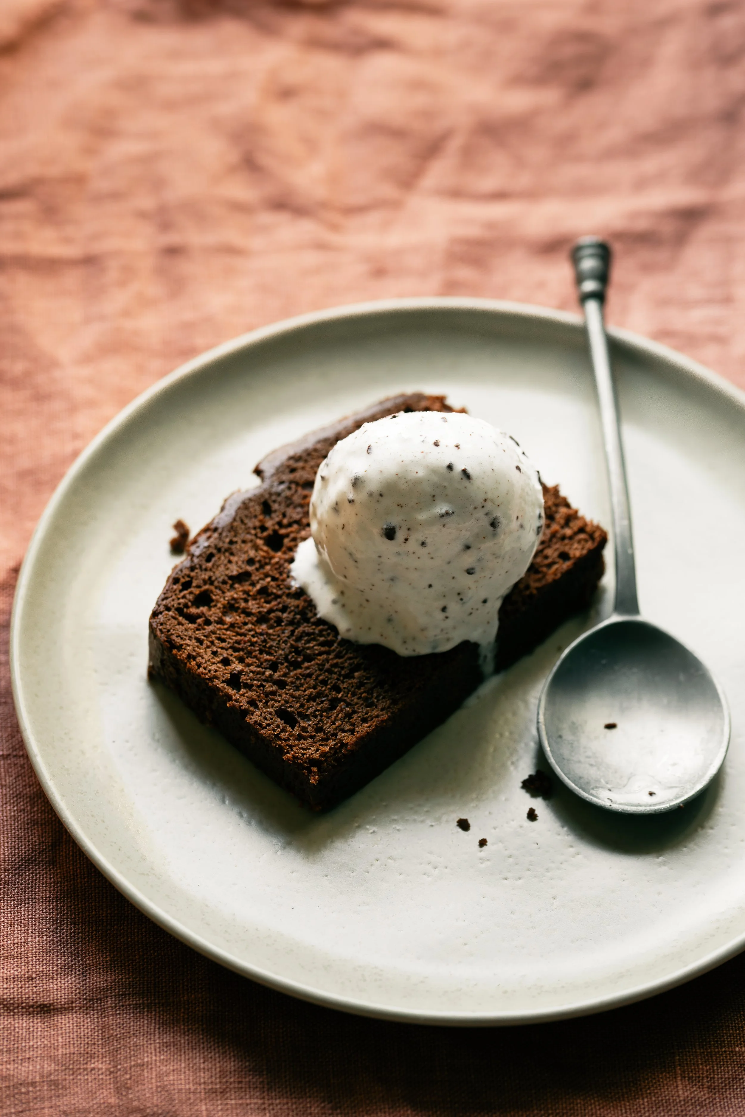 Chocolate cake with a scoop of vanilla ice cream on top, served on a white plate with a spoon.