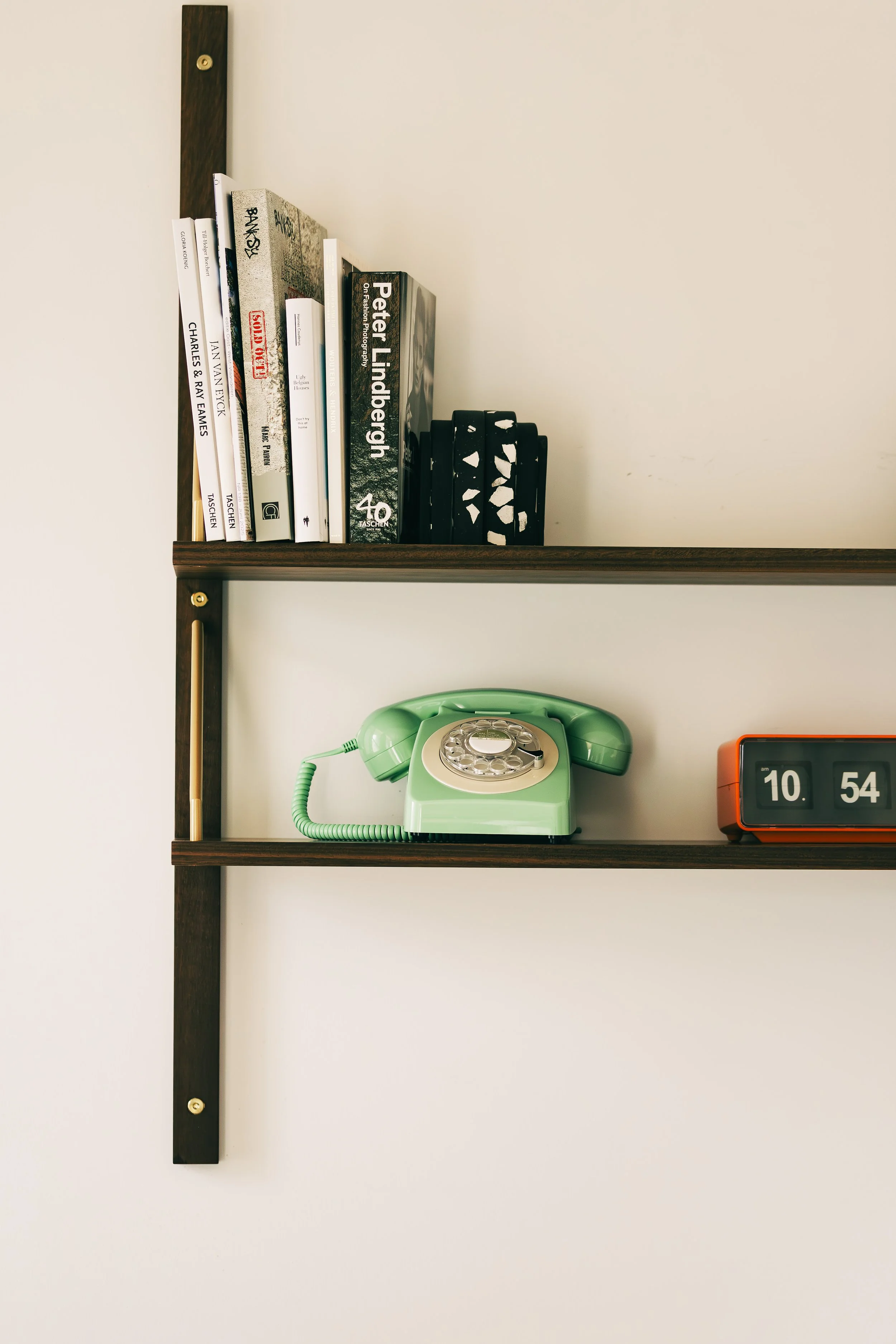 Wall shelf with books, a vintage green rotary phone, and a red flip clock showing 10:54.
