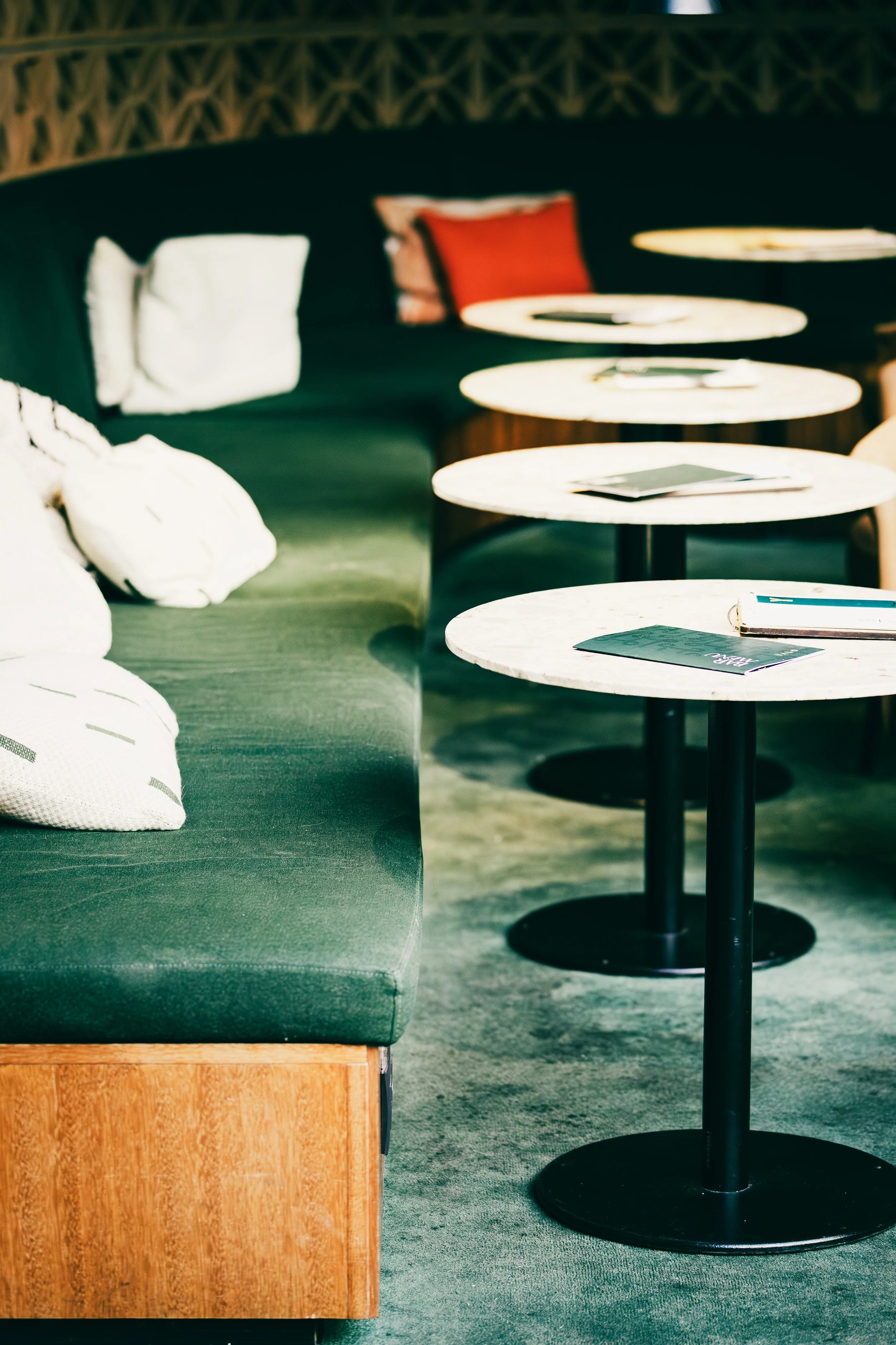 A row of small round tables with books on top, and a sofa with white and colored pillows in a cozy, modern space.