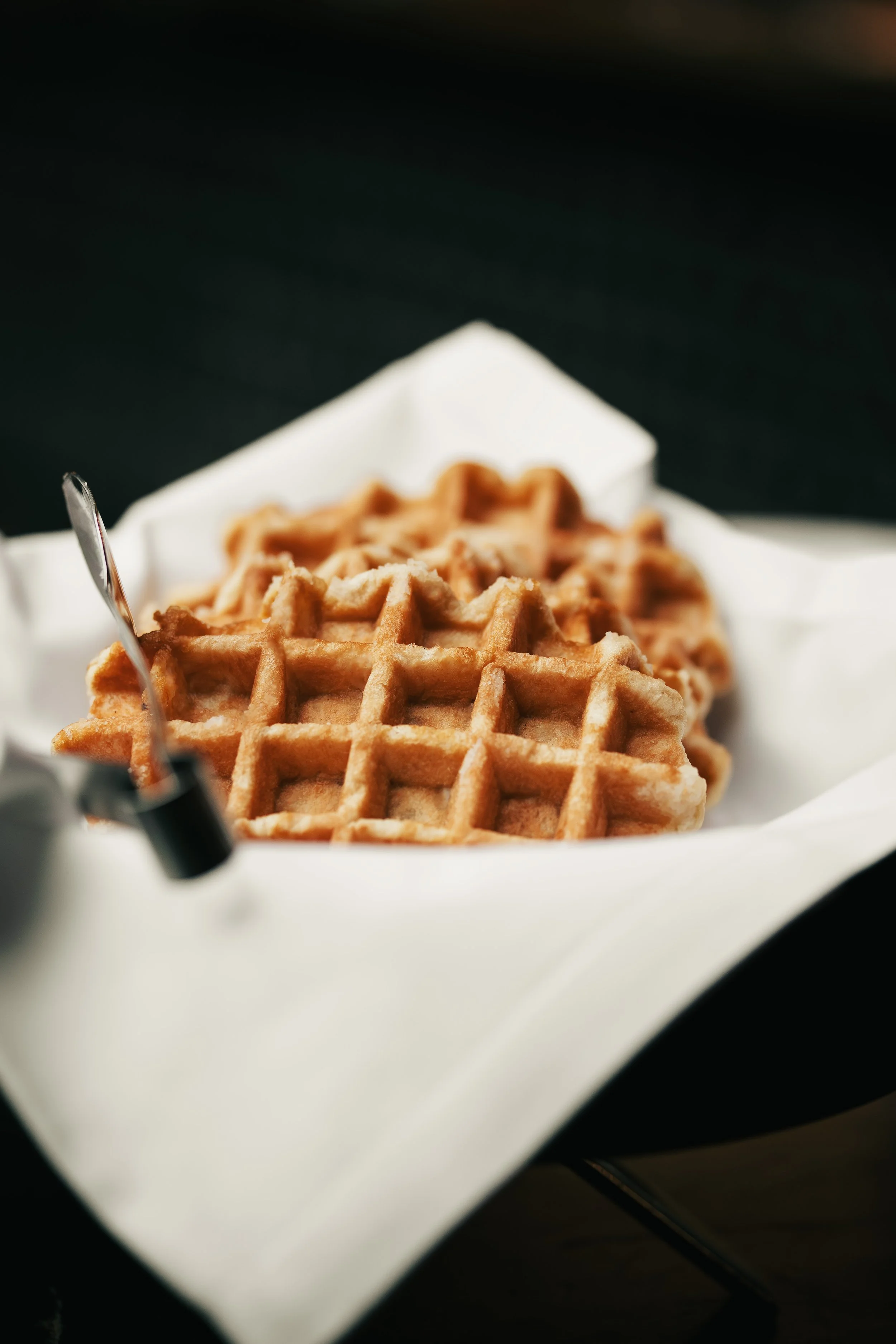 Close-up of two golden-brown waffles in a white basket lined with parchment paper.