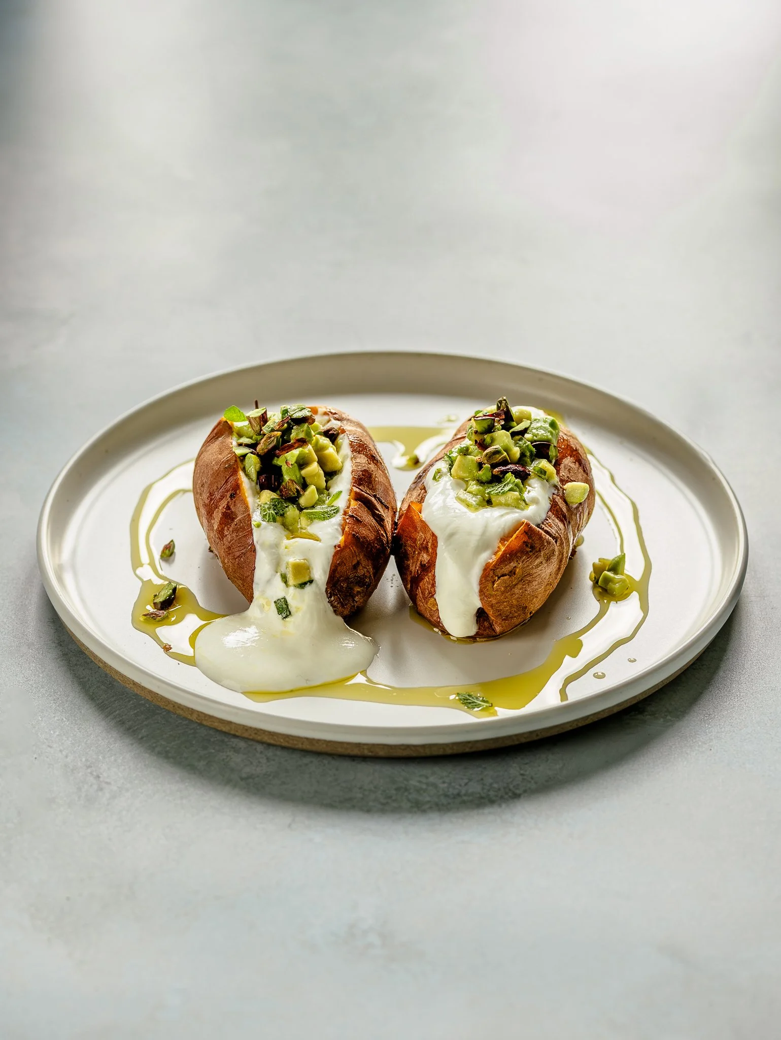Baked sweet potatoes topped with yogurt, chopped pistachios, and drizzled with honey, served on a white oval plate.